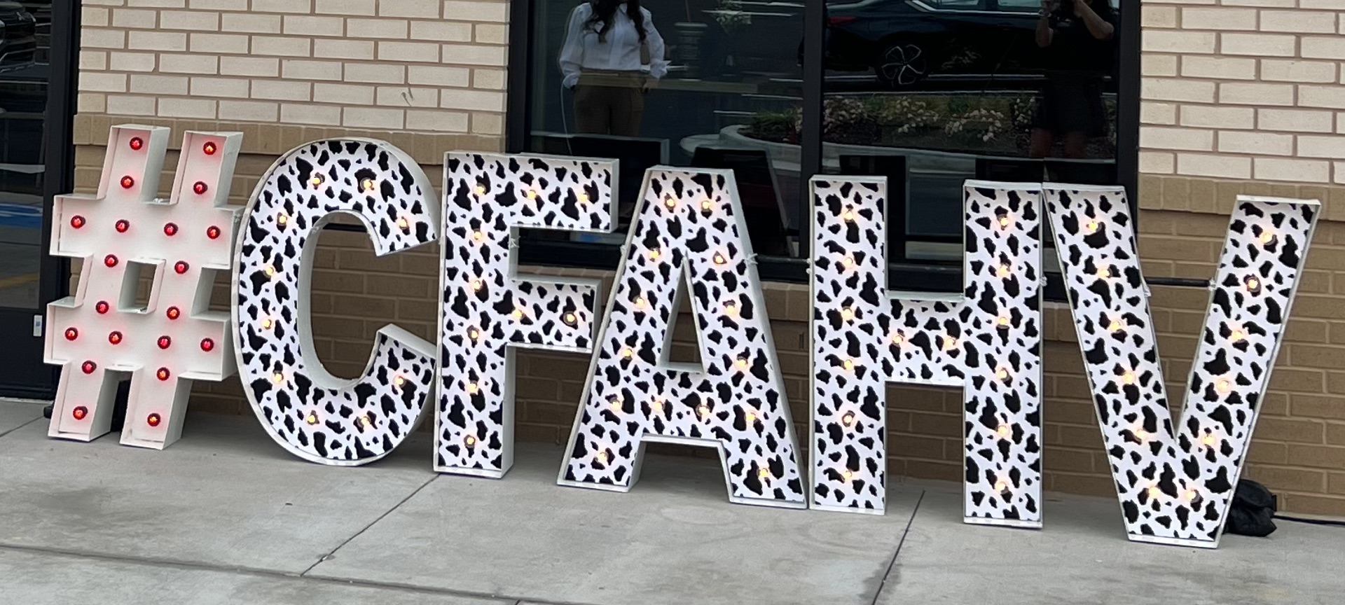 Lit letters spelling HVMS in front of silver and blue balloons at Hardin Valley Middle School with mural stars and music notes on the wall.