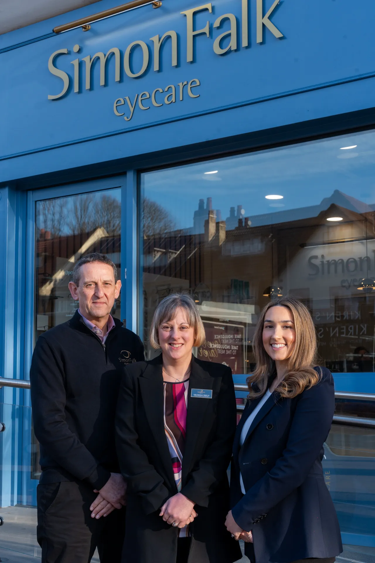 Three staff members posing in front of Simon Falk Eyecare storefront