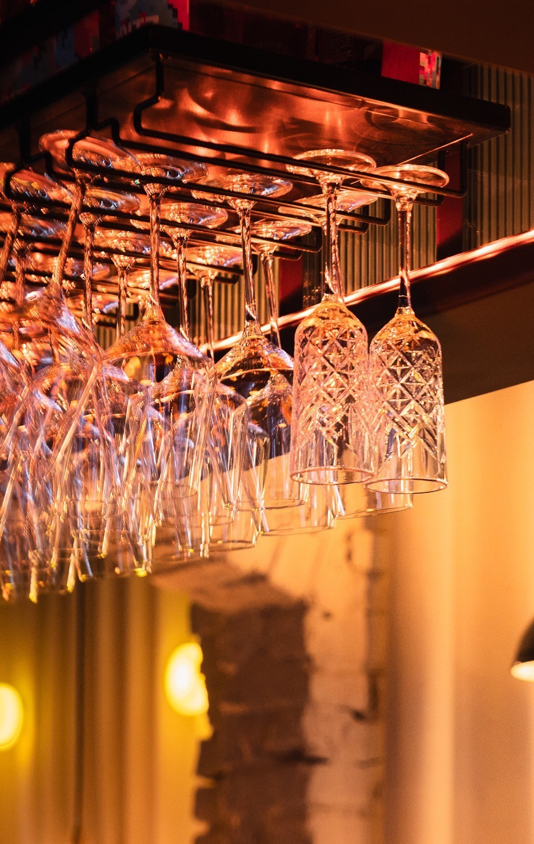 Rows of hanging crystal wine glasses with warm ambient lighting in a bar setting.