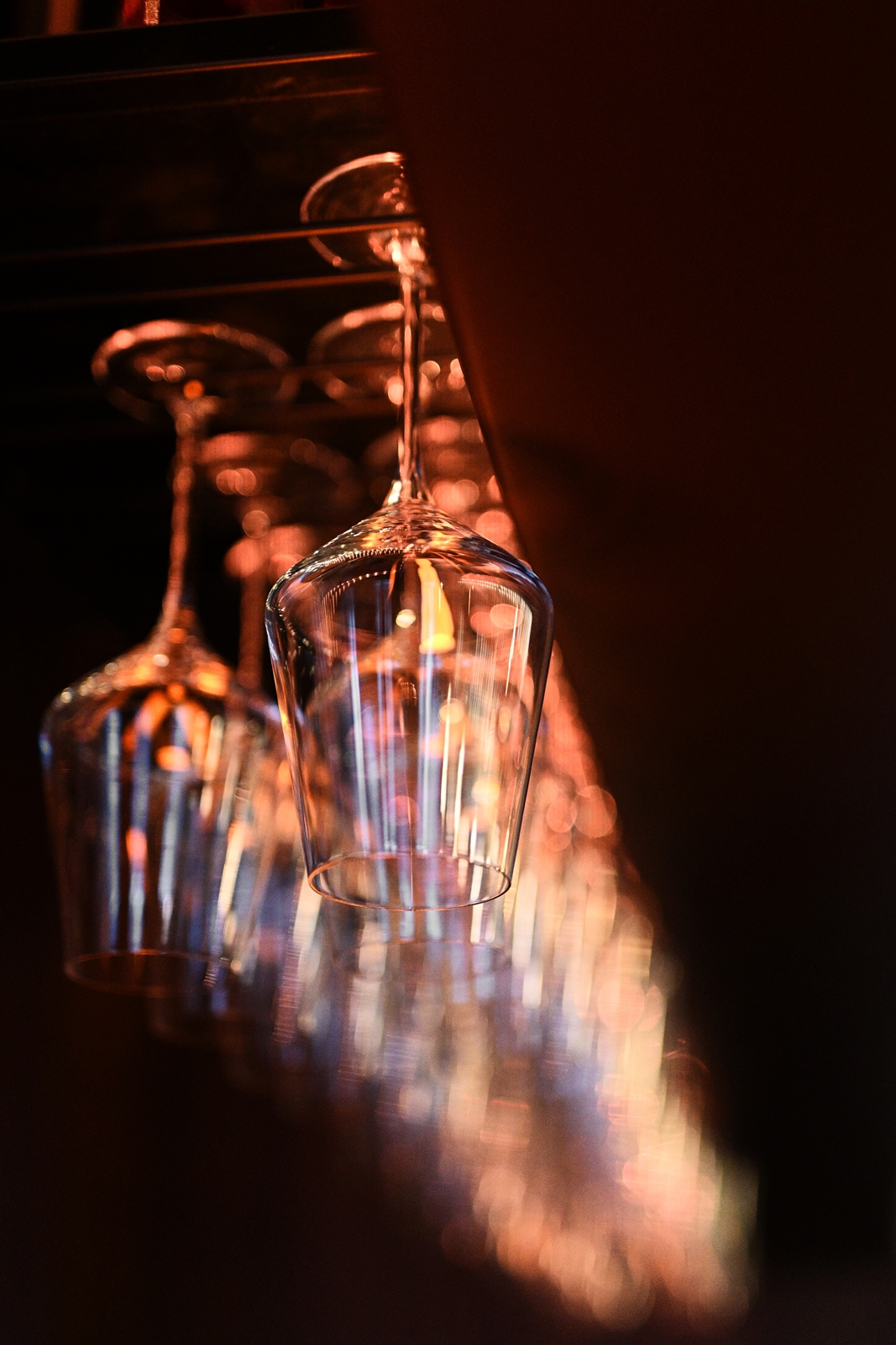 Rows of hanging crystal wine glasses with warm ambient lighting in a bar setting.
