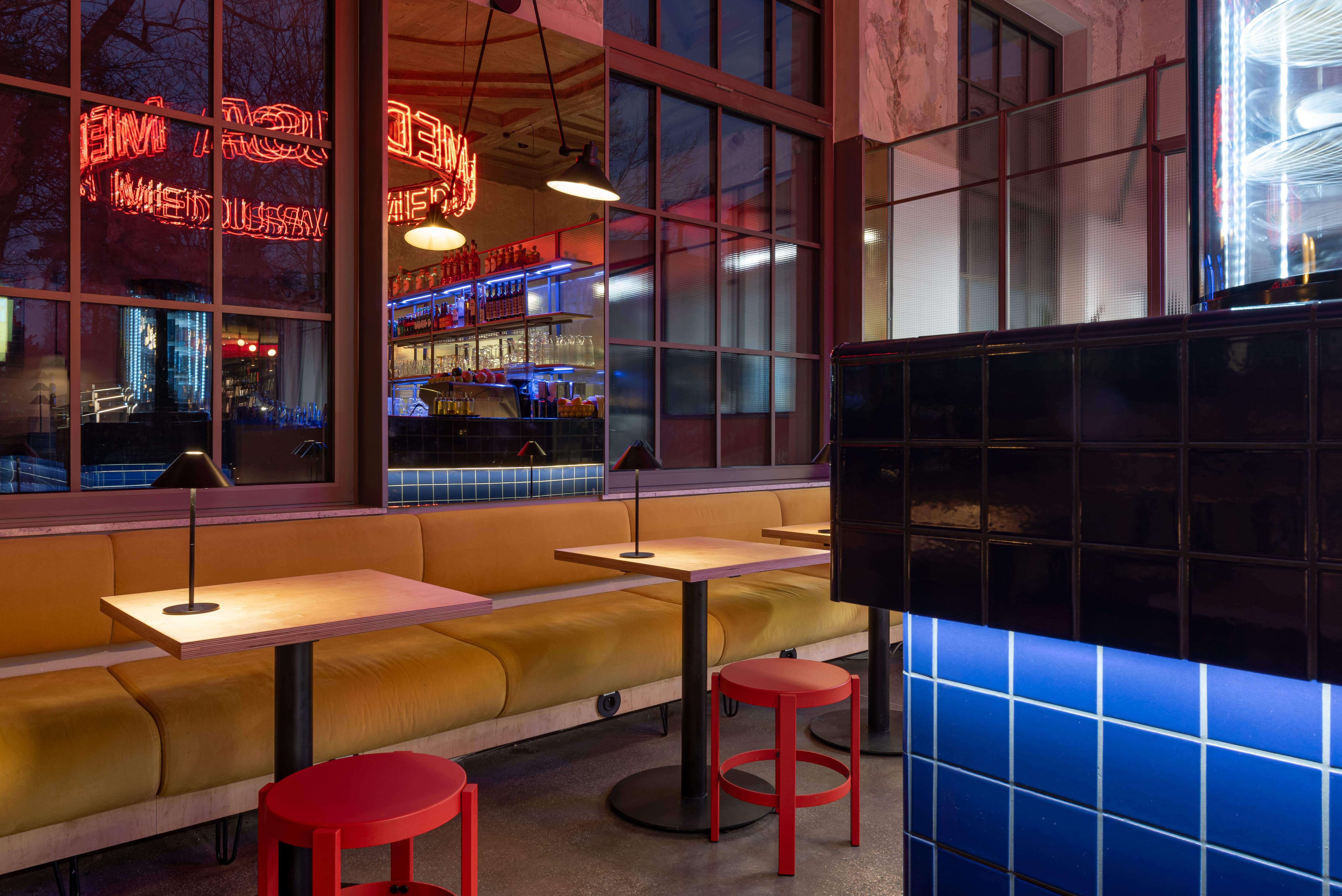 Modern bar with blue tiled counter, neon Medusa sign, and shelves of bottles and glasses.