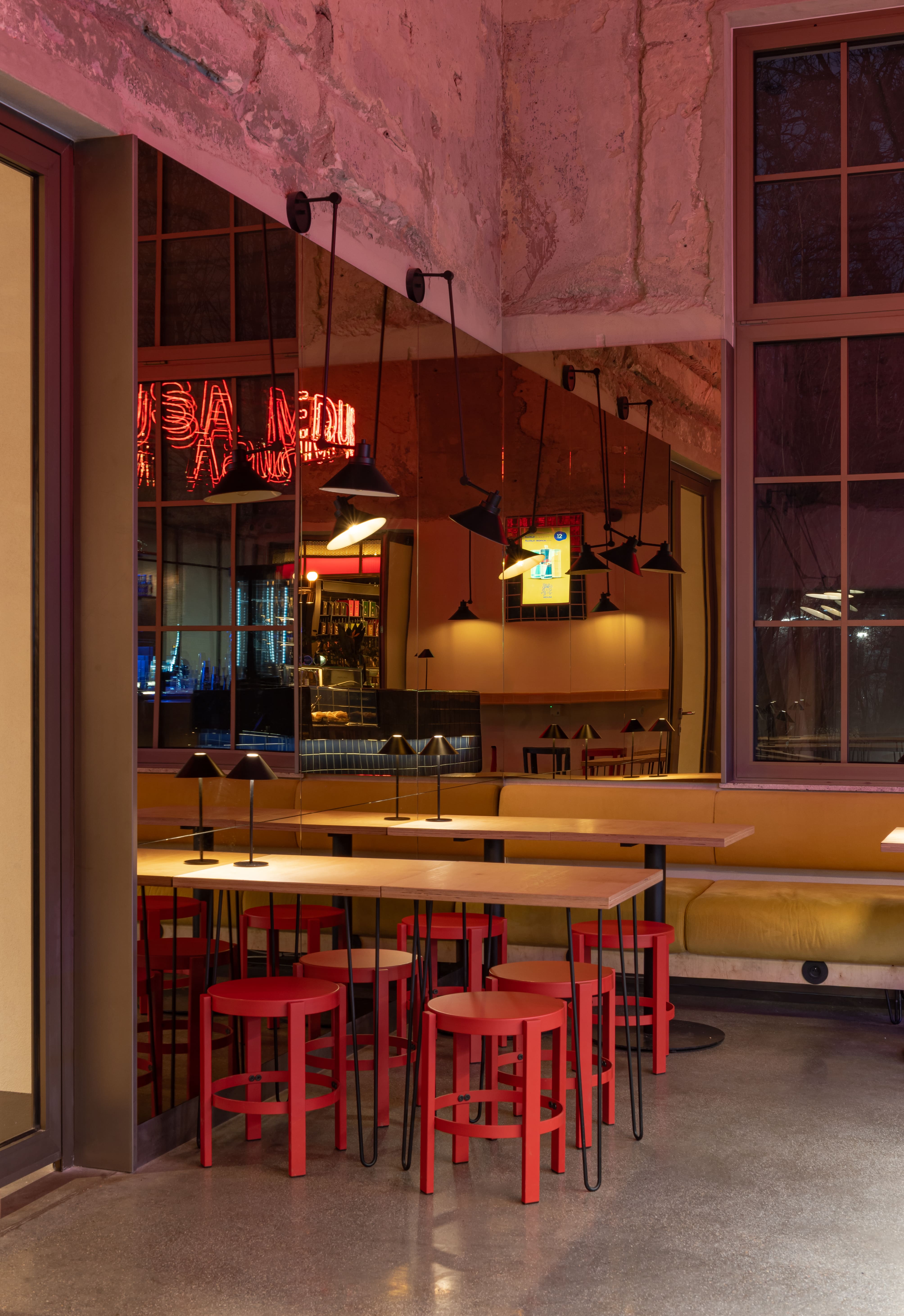 Indoor seating with red stools, wooden tables, yellow cushioned bench, and pendant lamps in a modern cafe.