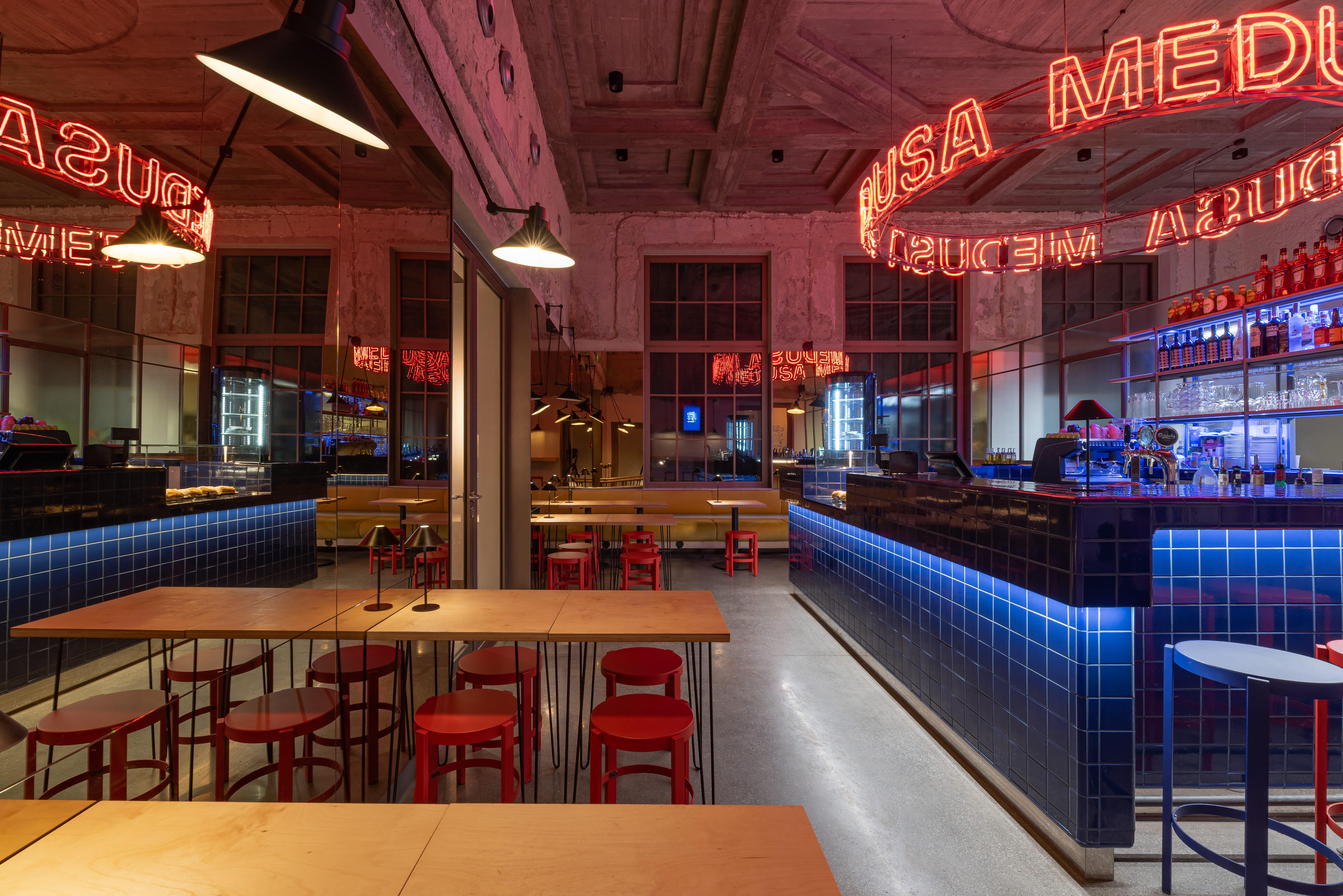 Modern bar interior with blue tile counter, red stools, wooden tables, and red neon circular sign.