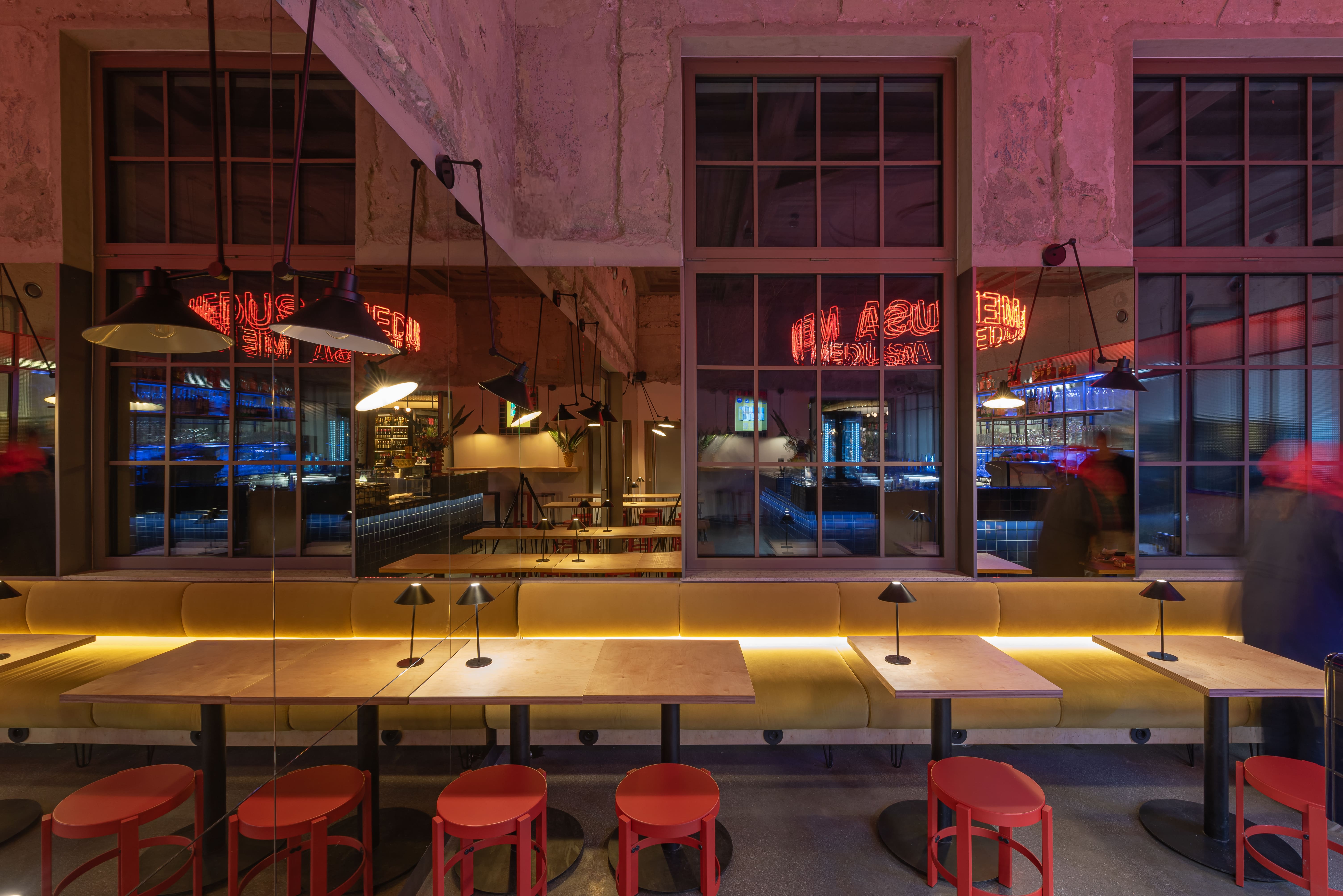 Modern bar with blue tiled counter, neon Medusa sign, and shelves of bottles and glasses.