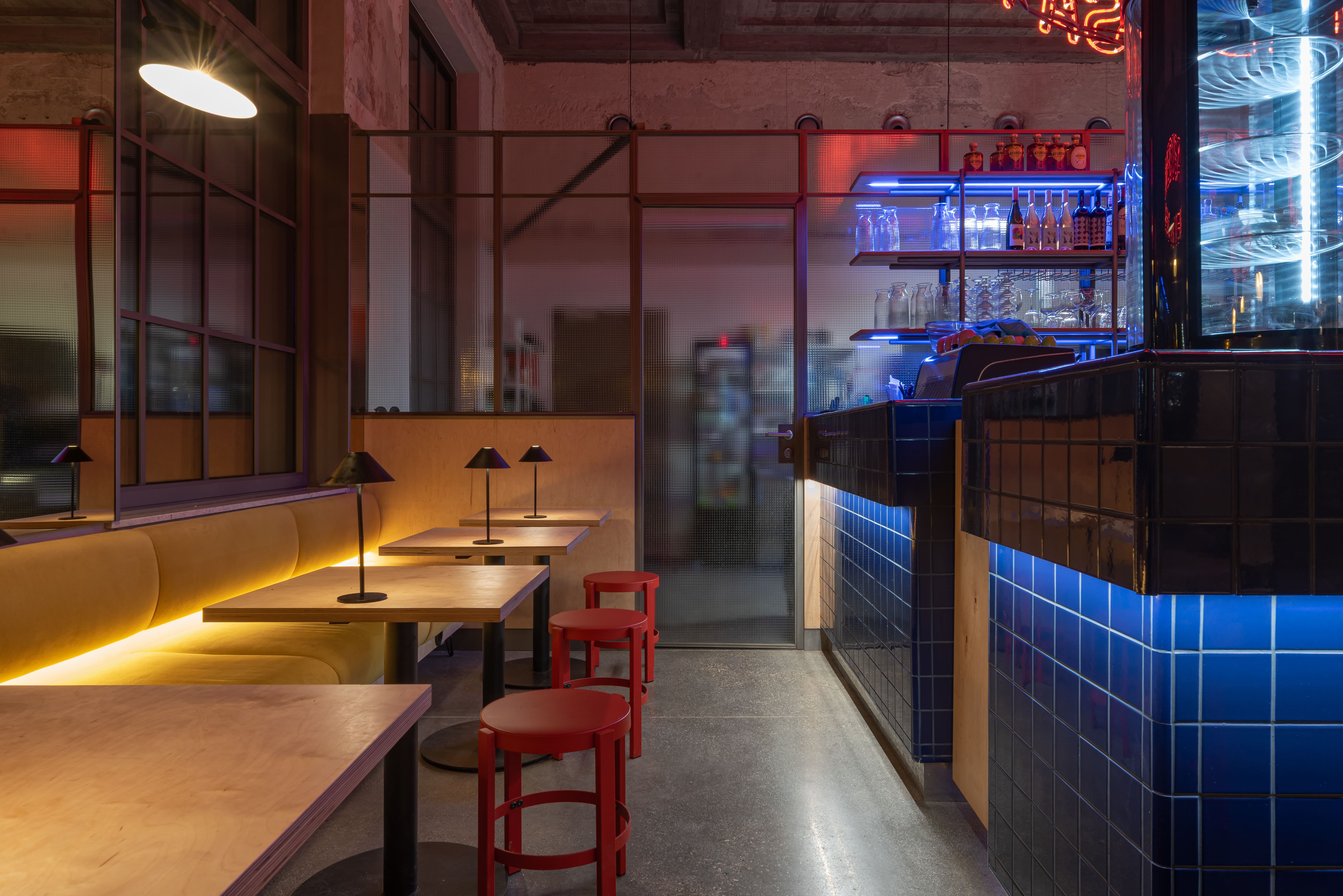 Modern bar with blue tiled counter, neon Medusa sign, and shelves of bottles and glasses.