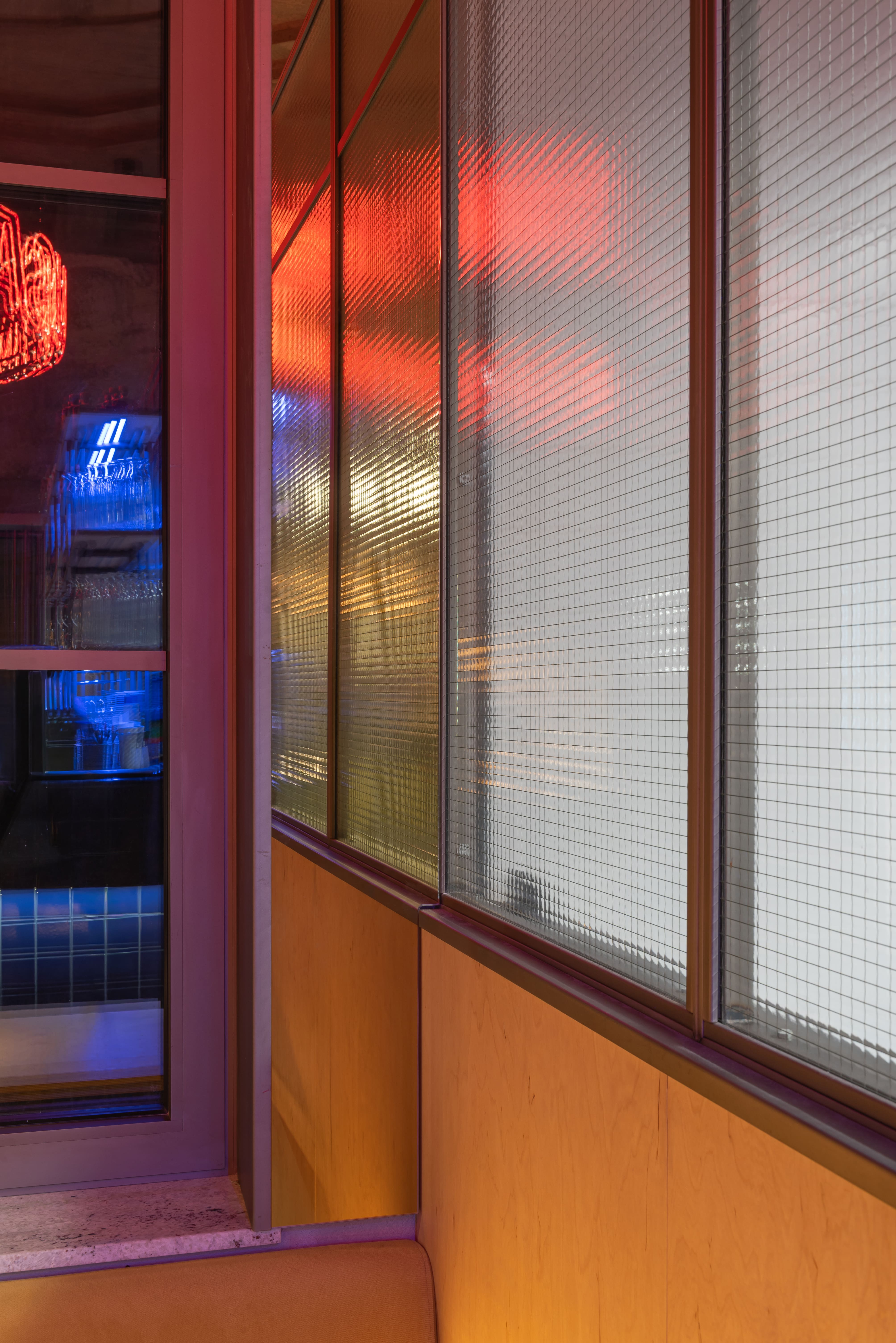 Interior of a bar with a neon circular sign reading 'MEDUSA', five tall stools, and shelves stocked with bottles and glassware.