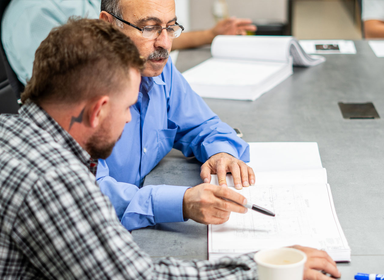 Two men discussing plans on a technical drawing