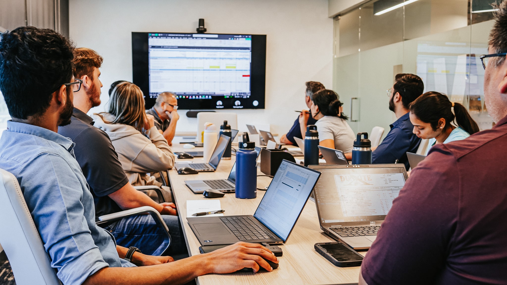 A meeting in a conference room with people on their laptops observing a presentation