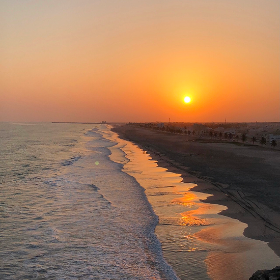 Sunset over a sandy beach with orange reflections on the water and gentle waves rolling in.