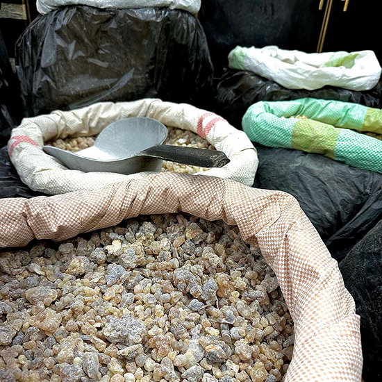 Close-up of large sacks filled with various dried resin or gum-like substances, with a metal scoop resting in one sack.