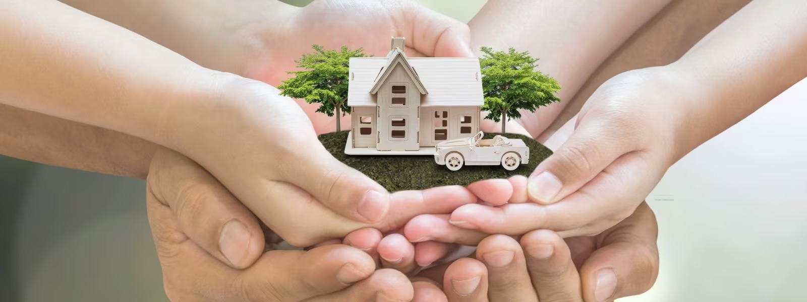 Family of hands holding miniature wooden house and car