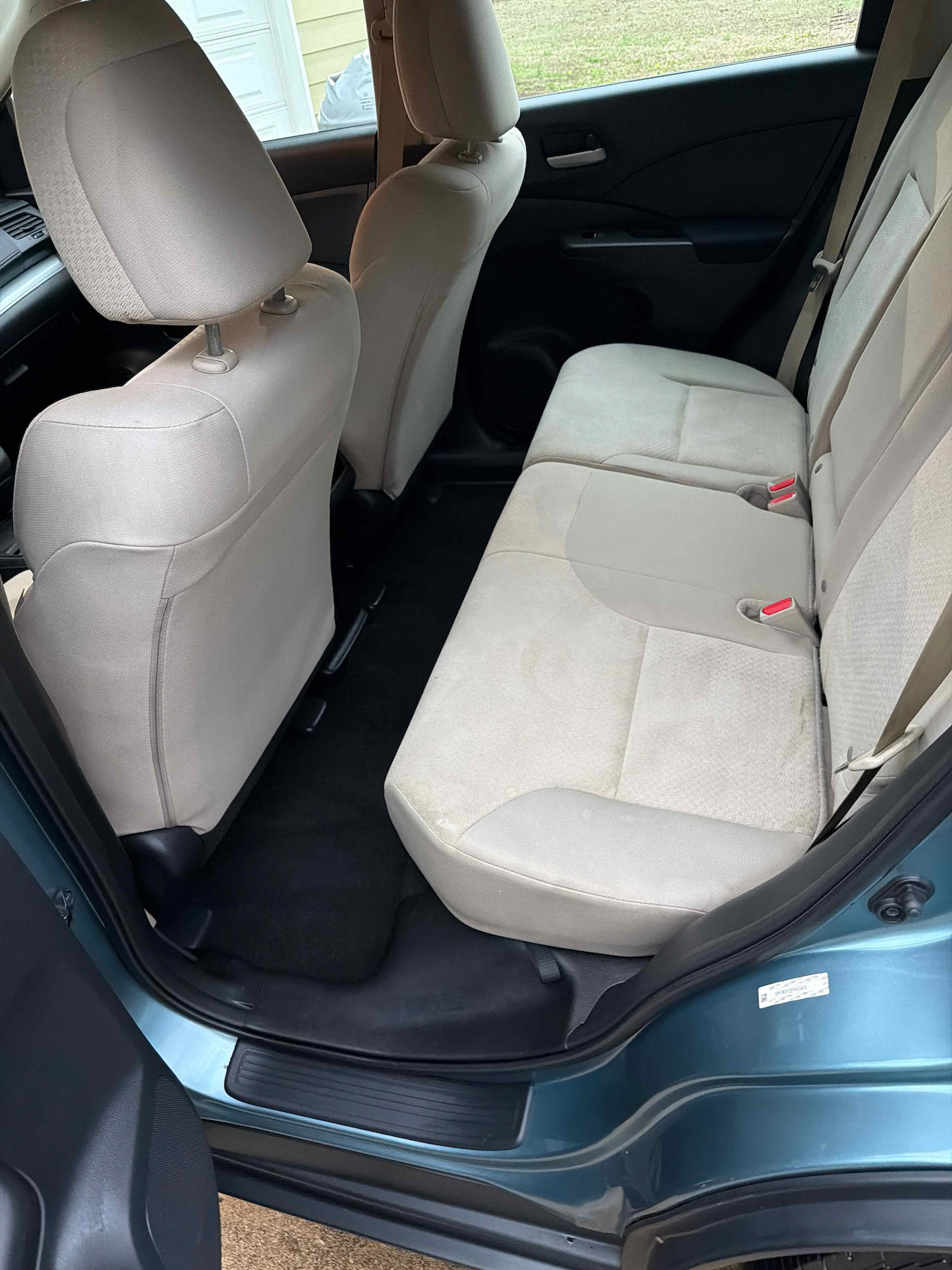 Interior of a car showing the rear passenger seats upholstered in light beige fabric with the door open.