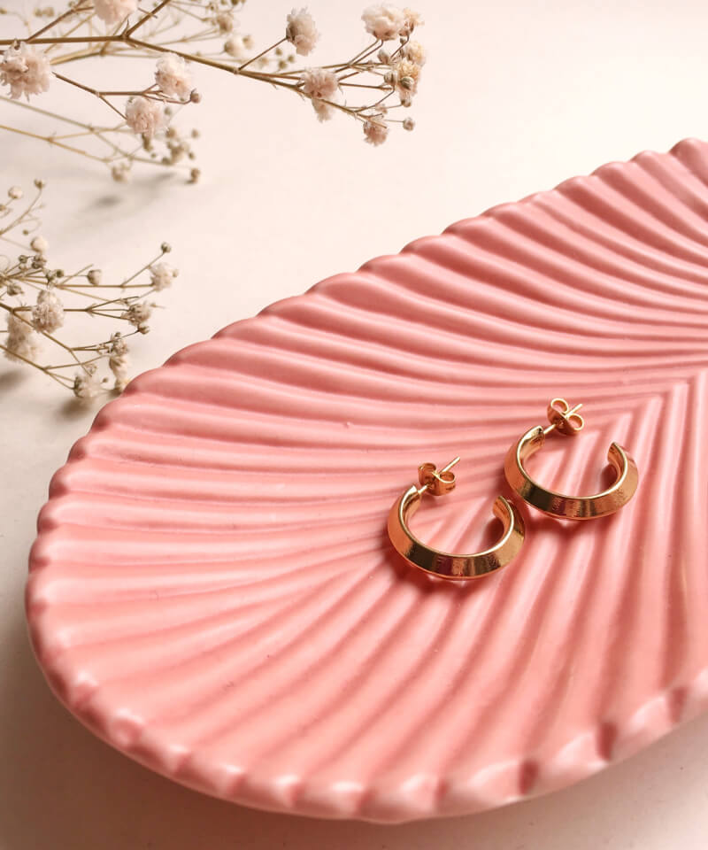 Gold hoop earrings on a pink shell