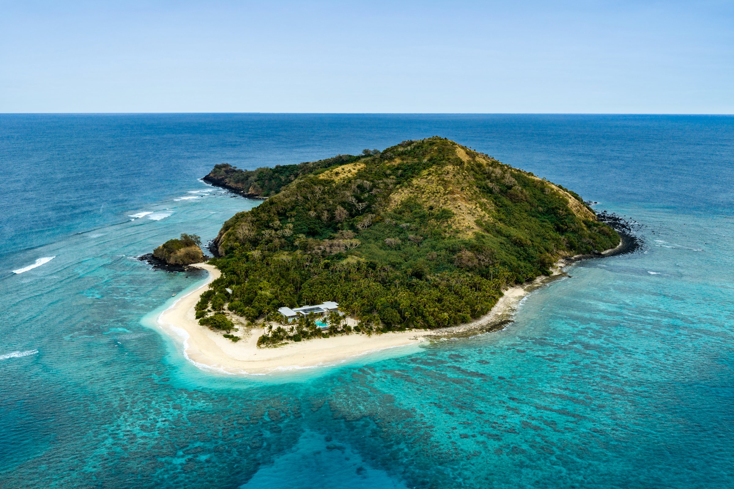 Aerial view of the private island ringed by turquoise reef and a long white sand beach