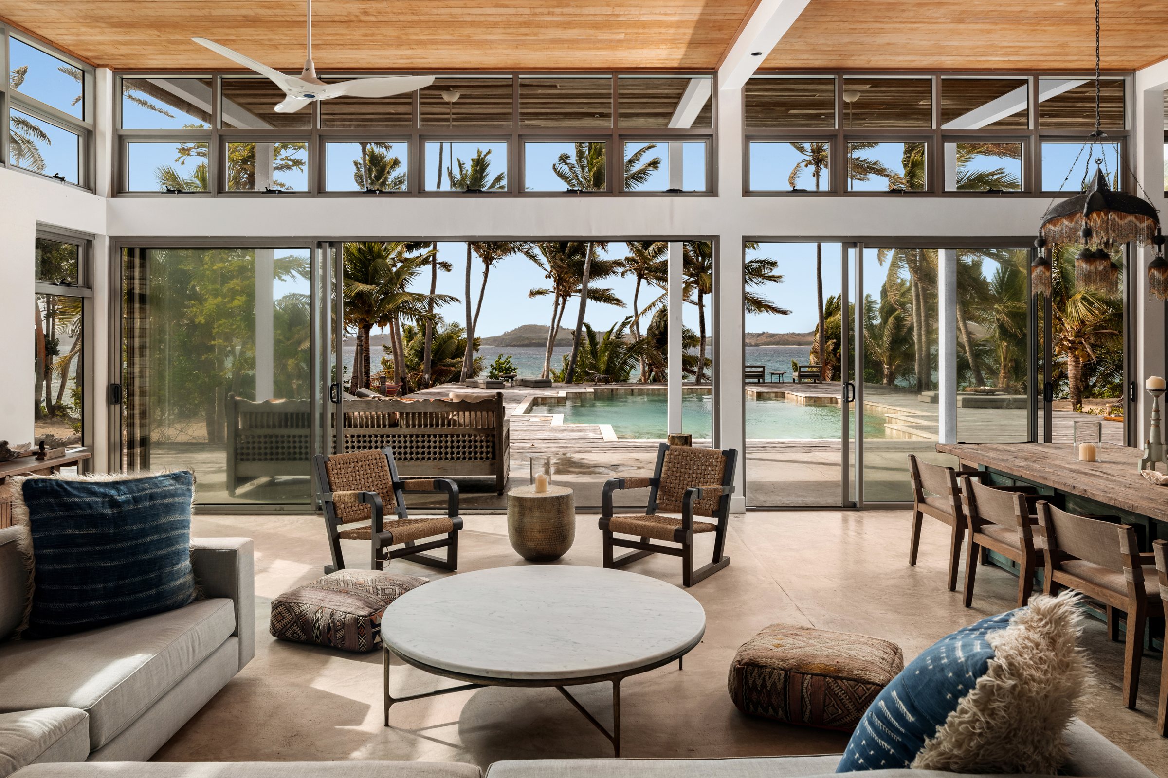 Lounge with woven chairs and a marble table, sliding doors open to the pool and ocean
