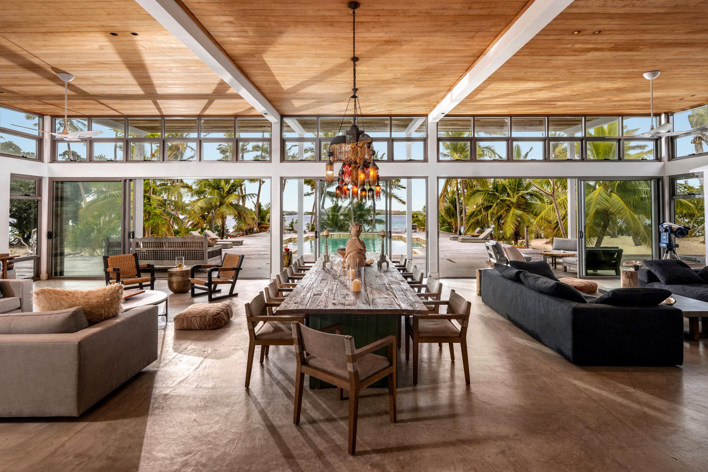 Great room with a long reclaimed timber dining table beneath a beaded chandelier, open to the pool