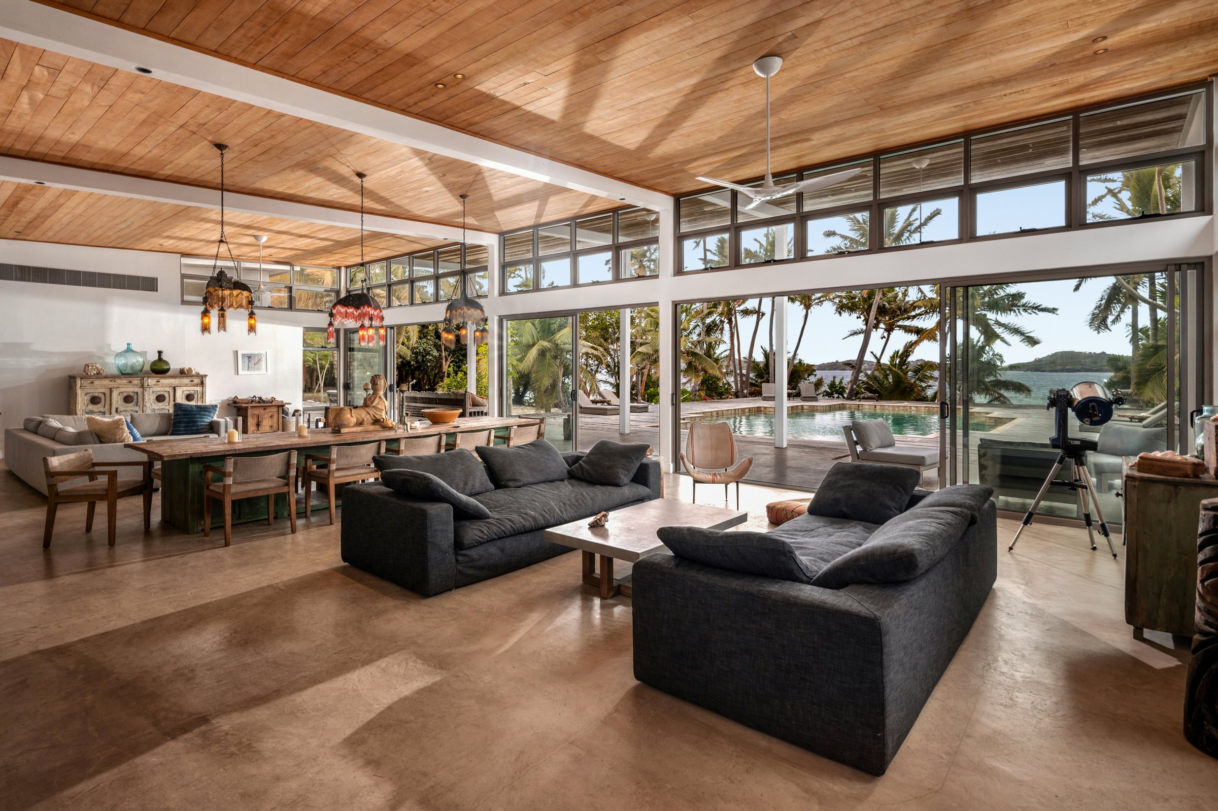 Living room with deep sofas and a telescope, glass walls opening to the pool and sea