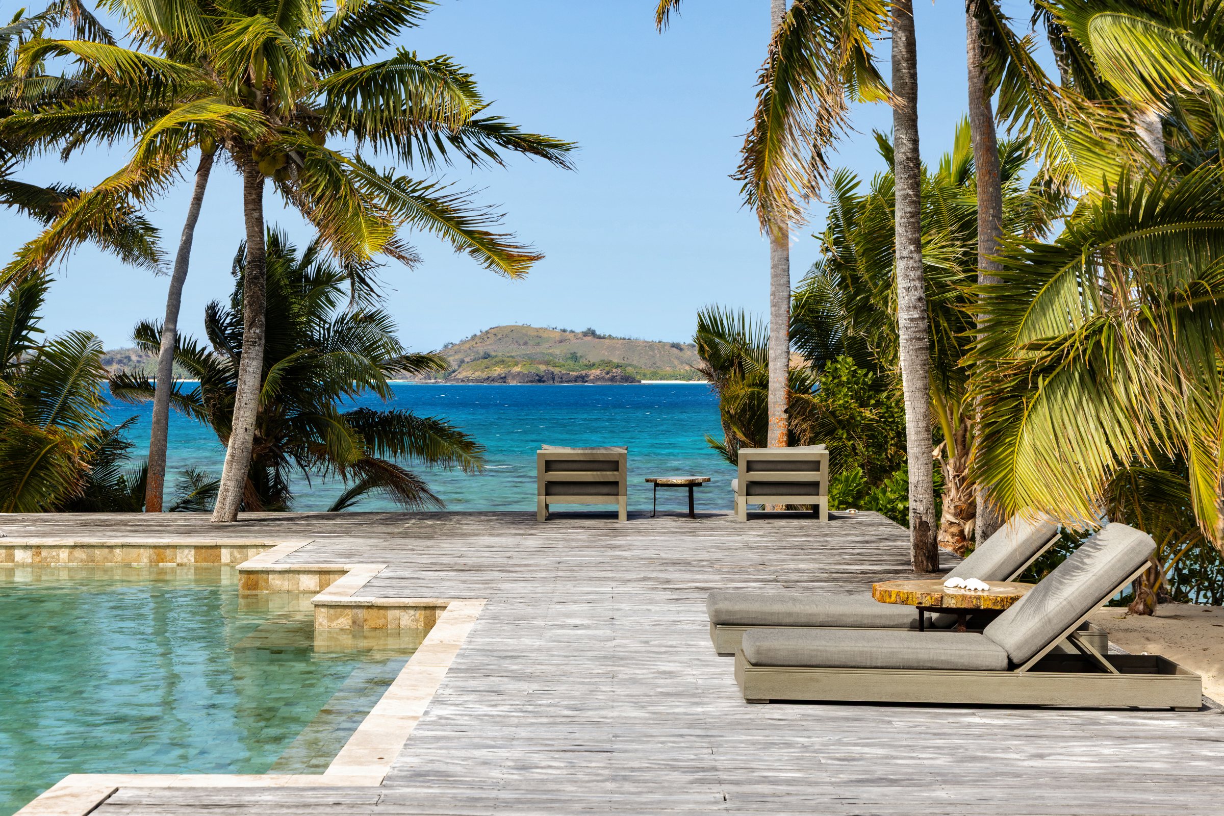 Pool deck with loungers and lounge chairs looking across turquoise water to a neighboring island