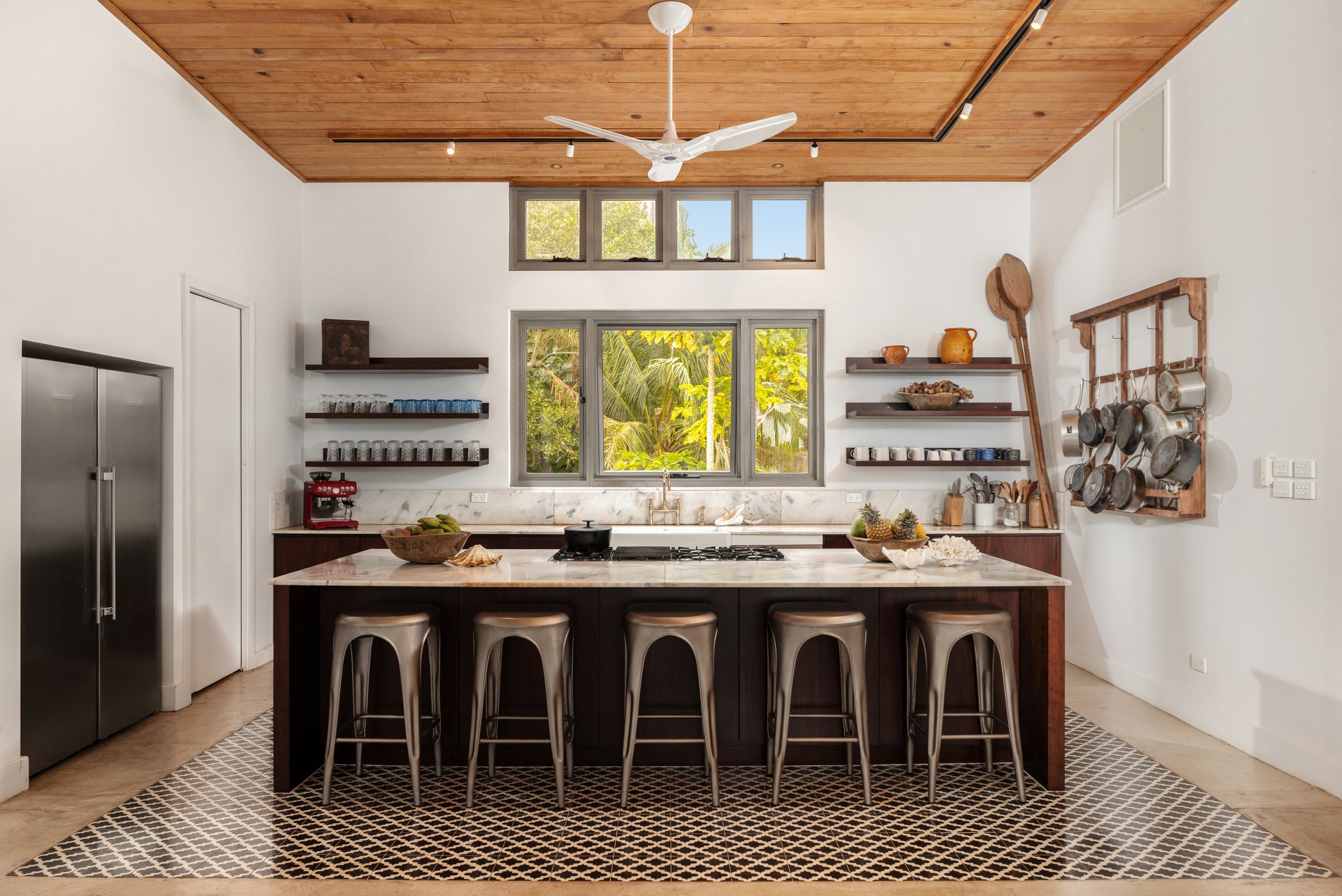 Kitchen with marble island, patterned tile floor, open shelving, and a window onto the palms