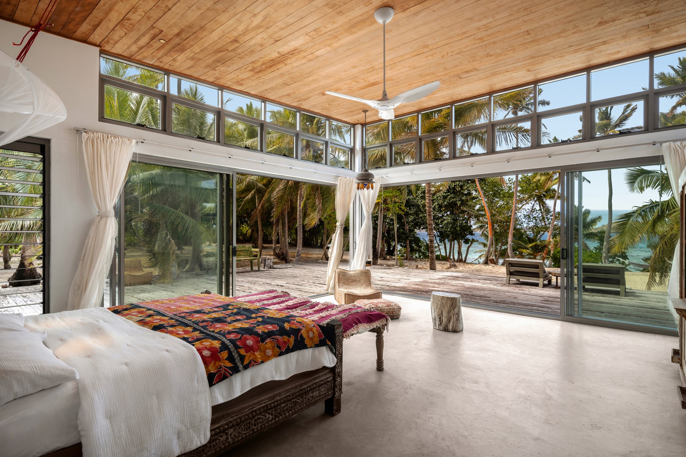 Bedroom with a carved bed and floral quilt, sliding doors open to the deck and sea