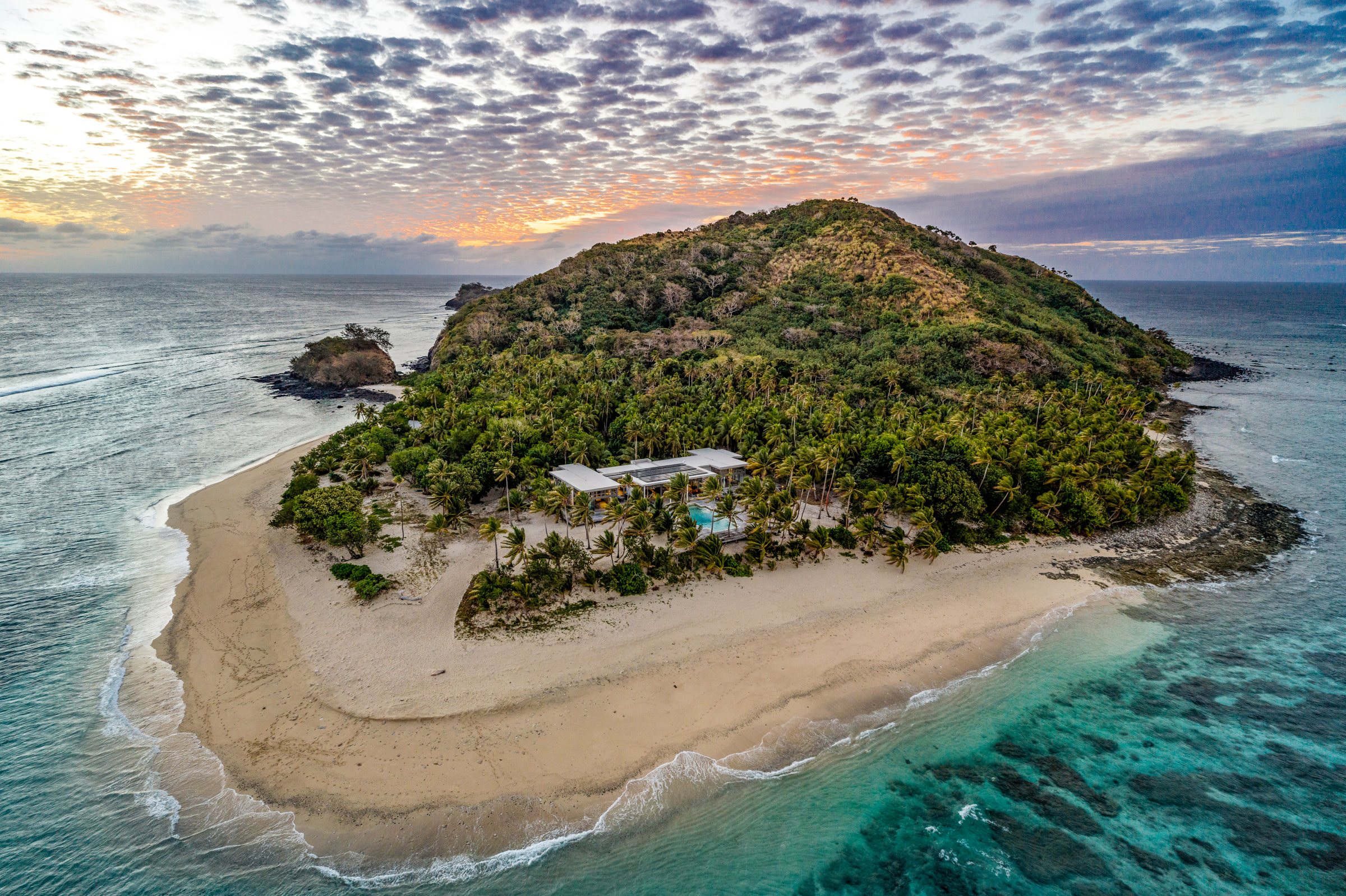 Close aerial view of the residence and pool among palms on the island's sandy point at dusk