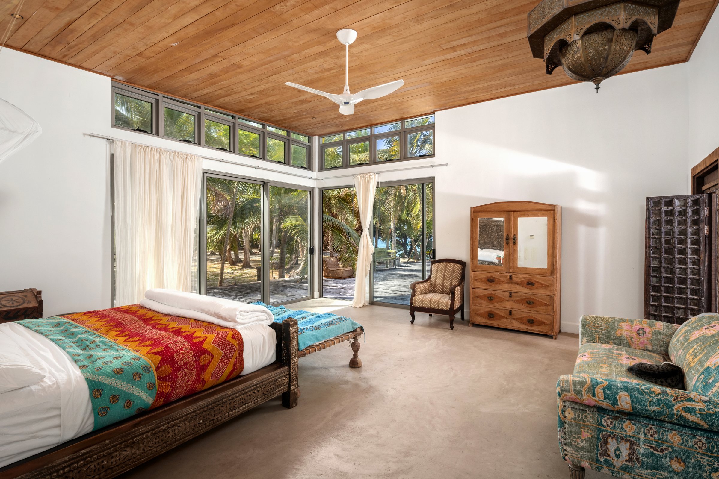 Bedroom with a colorful kantha quilt, antique armoire, and doors opening to the palm grove
