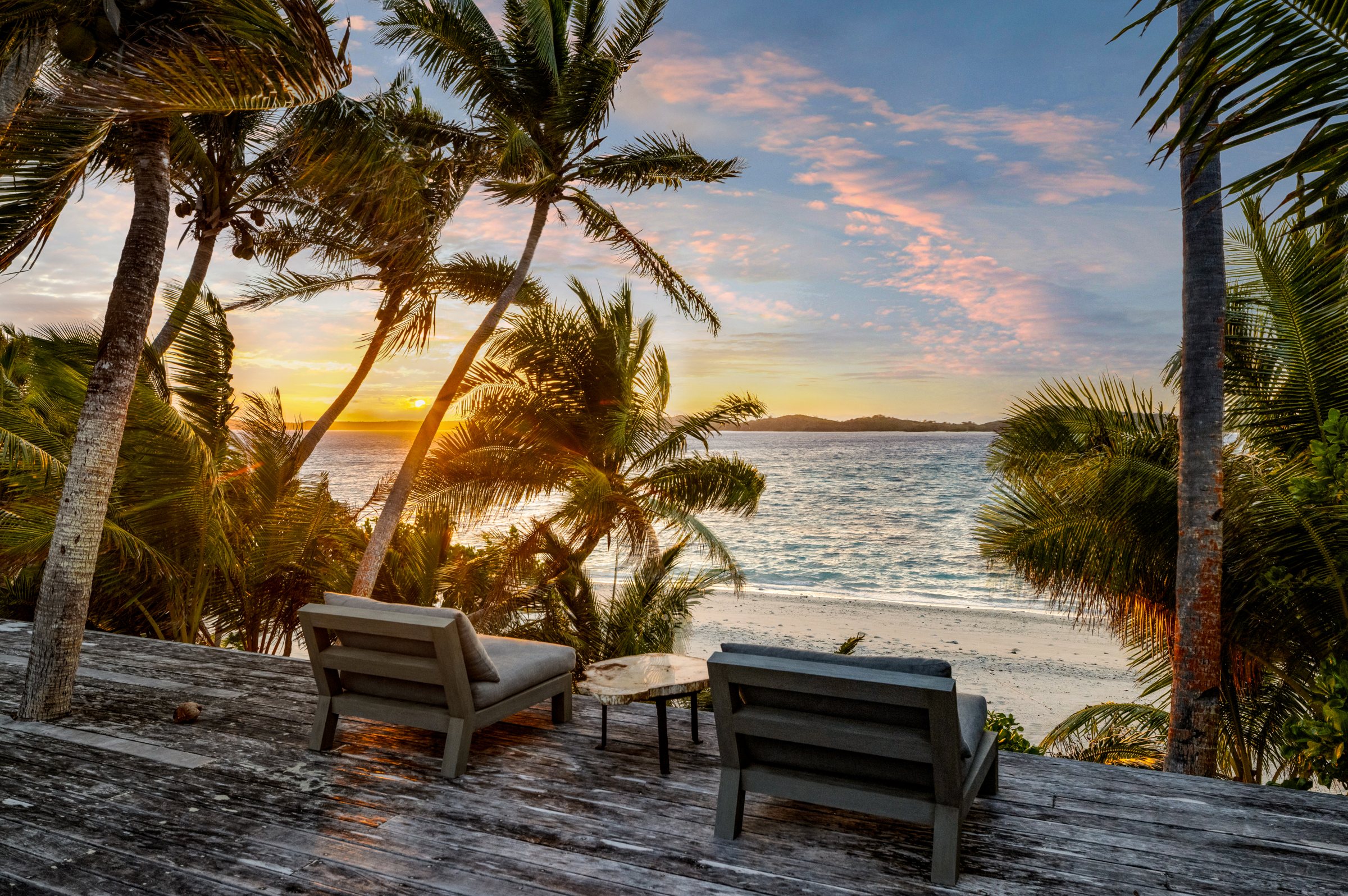 Two lounge chairs on the deck overlooking the beach and ocean at sunset