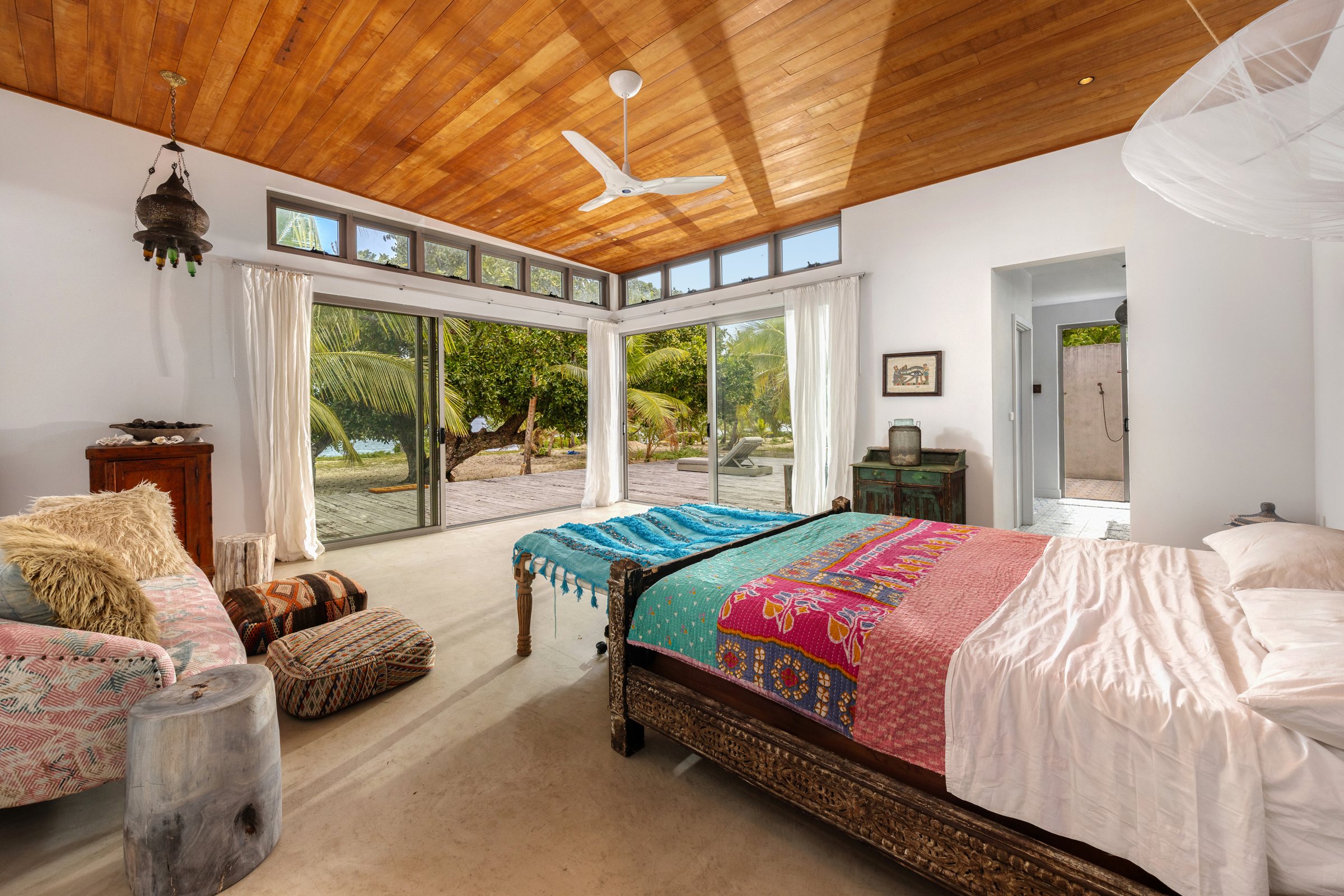 Bedroom with a carved bed and bright kantha quilt, doors open to the deck and shoreline