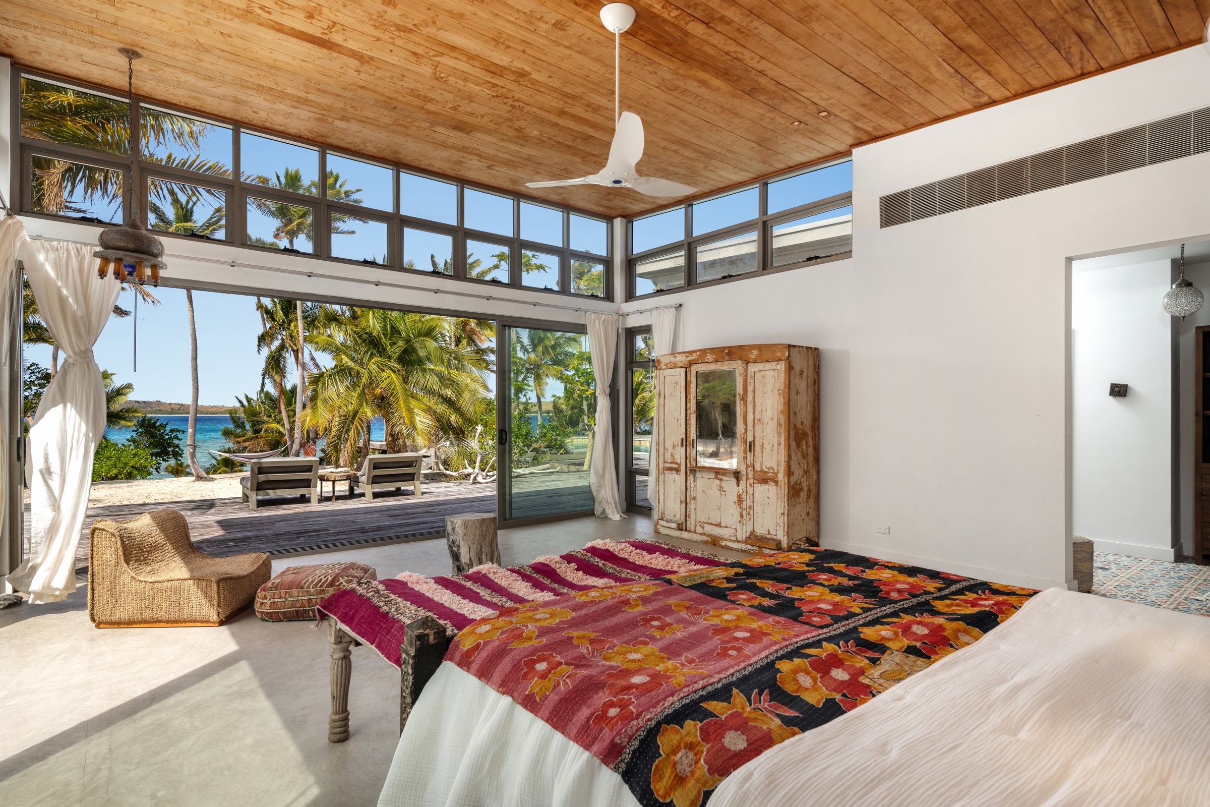 Bedroom with a floral quilt and vintage armoire, looking out to the beach through open doors