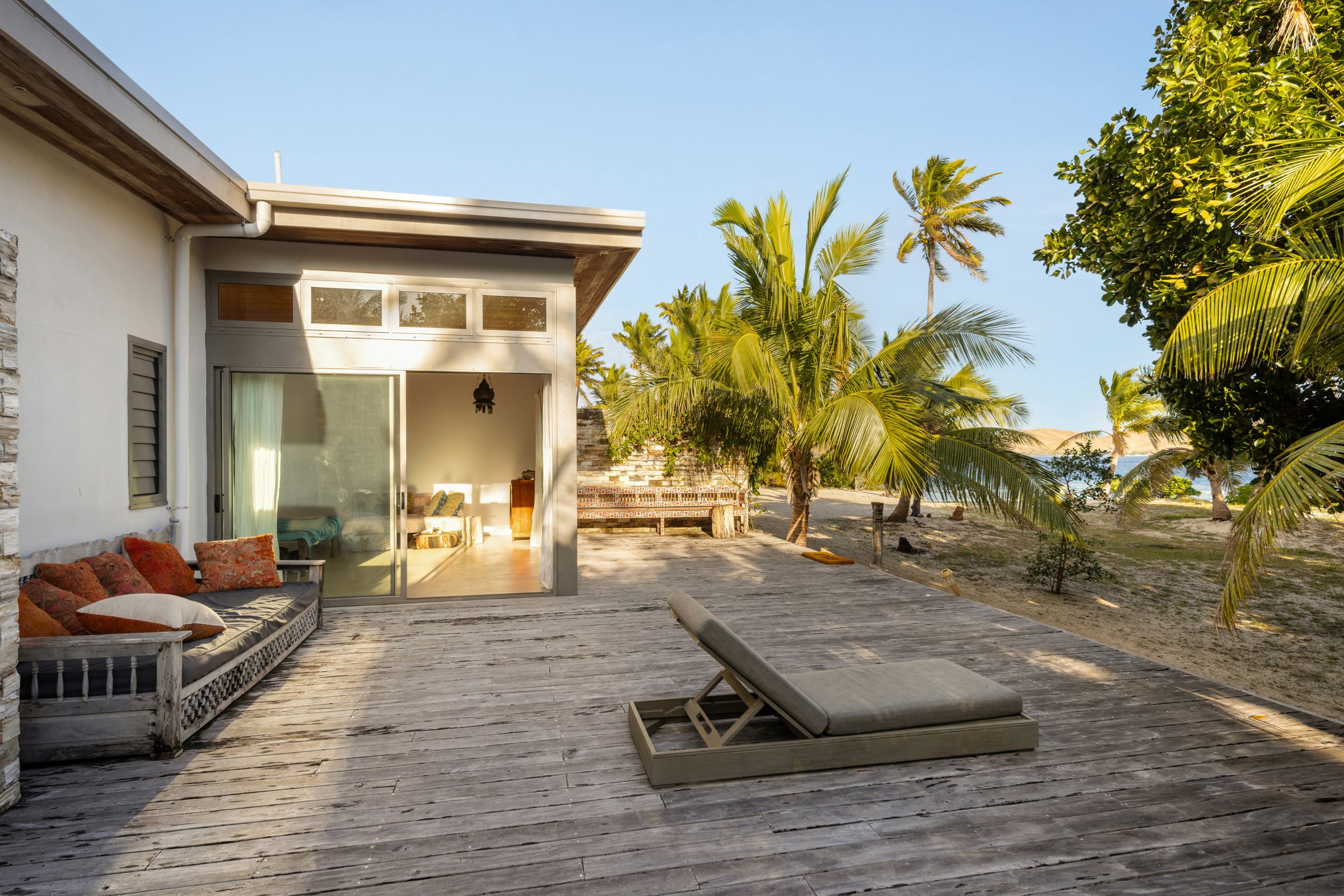 Timber deck with a daybed and lounger beside a suite, palms and the bay beyond