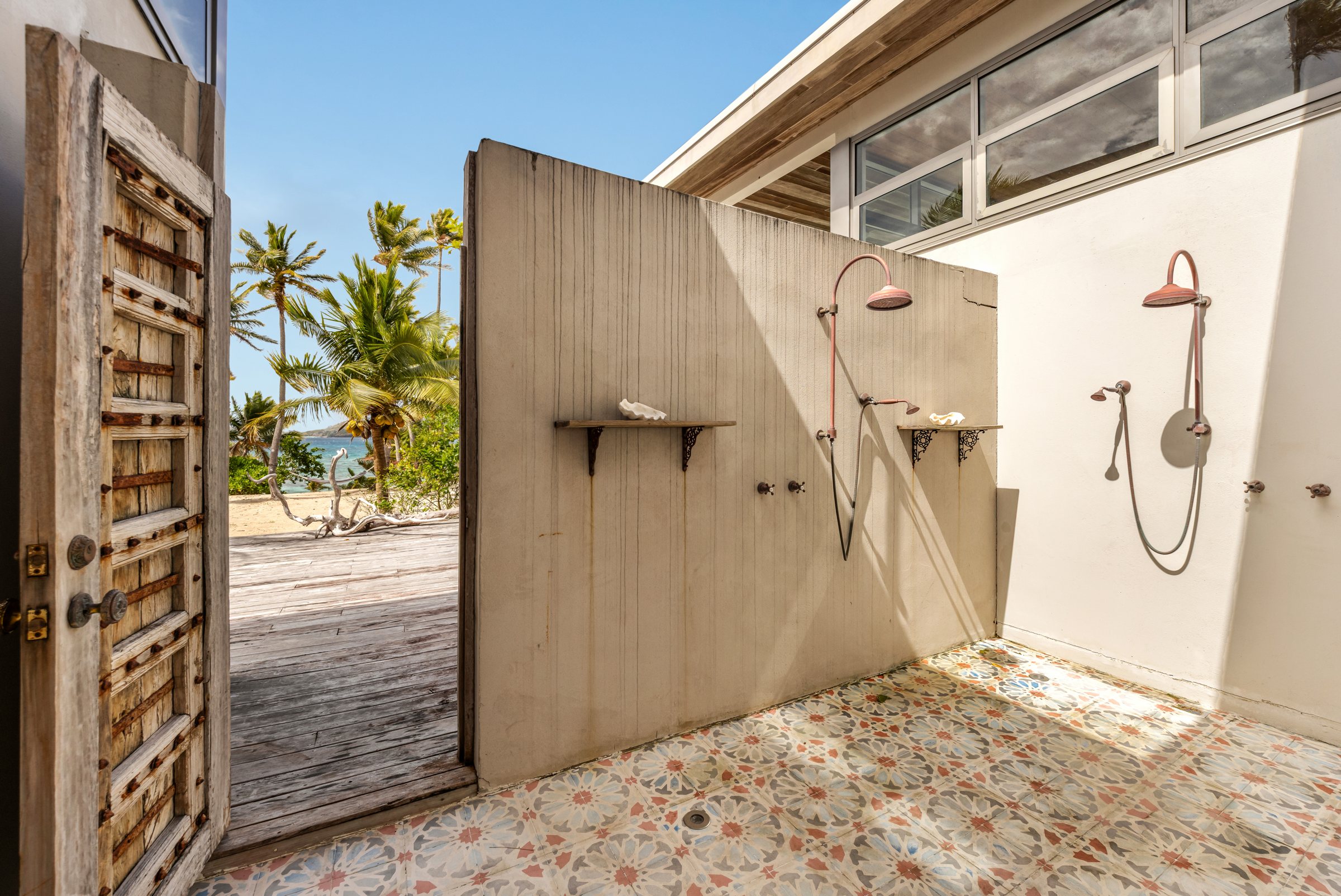 Open-air shower with copper rain heads and an antique door opening to the beach