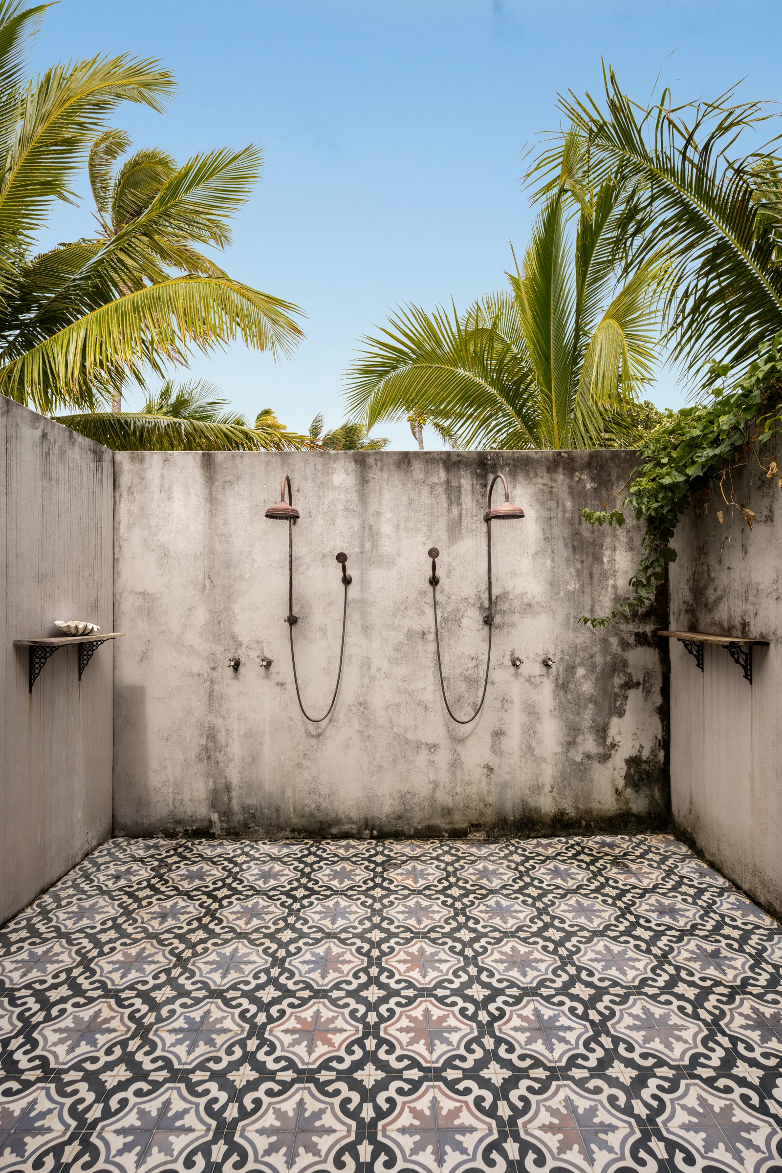 Open-air shower with copper rain heads and encaustic tile floor beneath palm trees