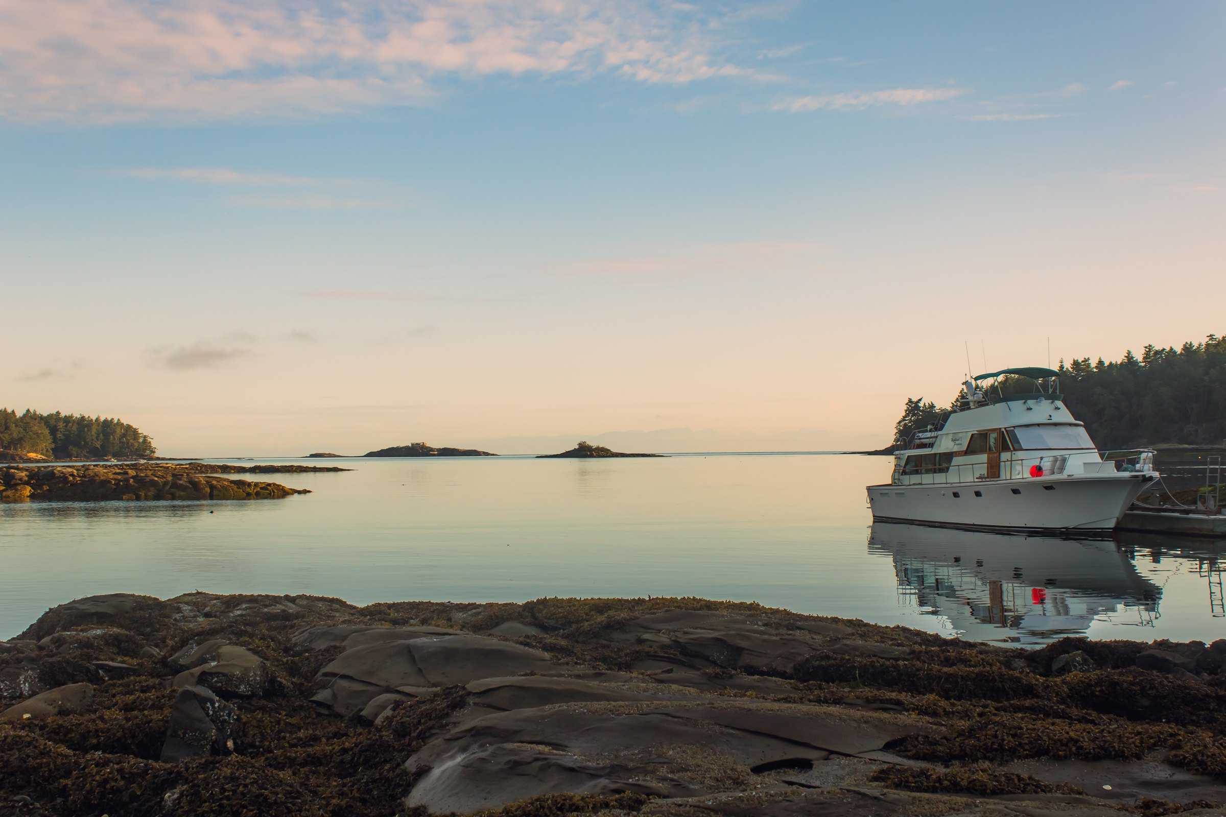 A yacht moored at the estate's dock on calm water at dawn, with forested islands across Whaler's Bay