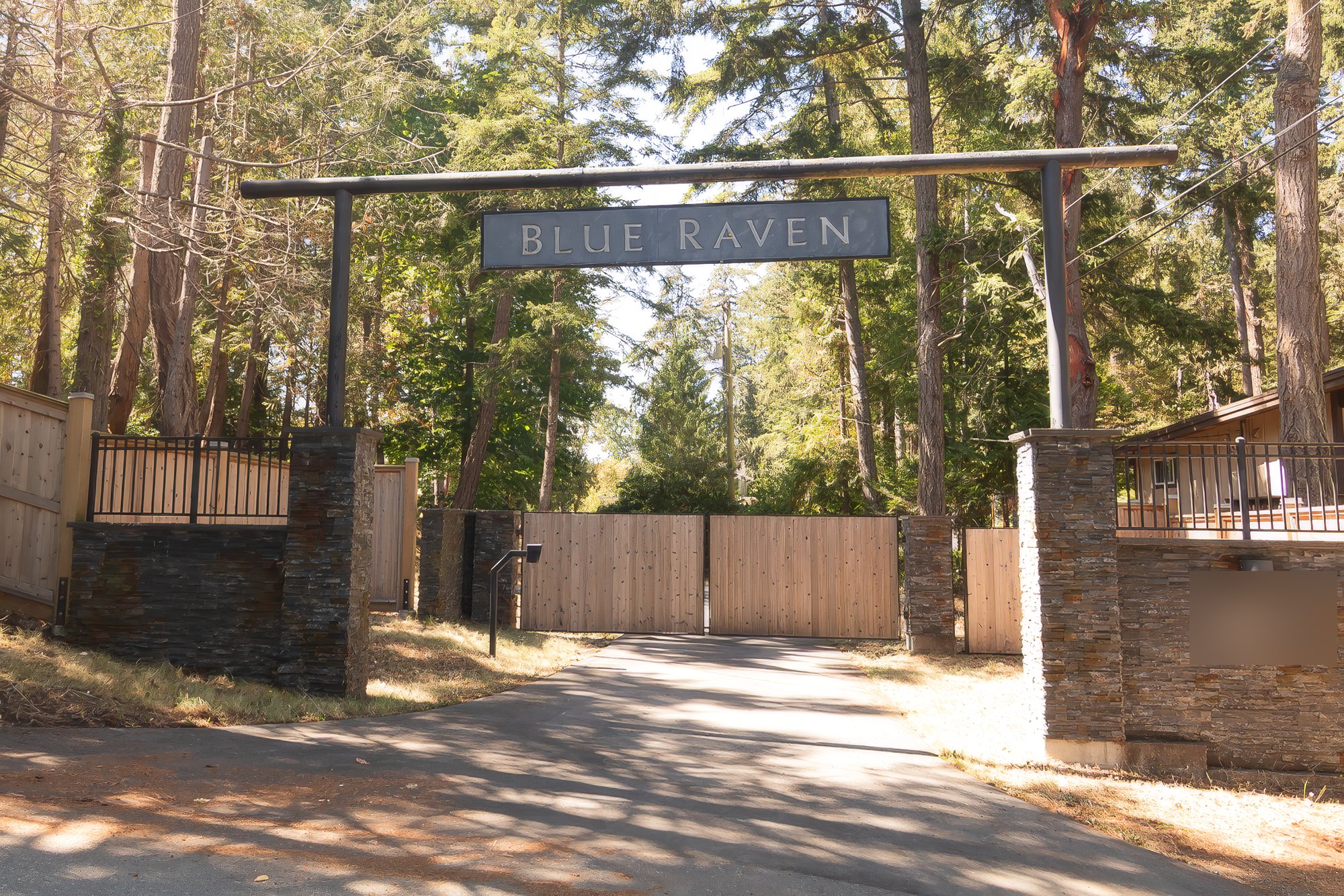 Timber arch signed Blue Raven over stone pillars and cedar gates at the wooded entrance