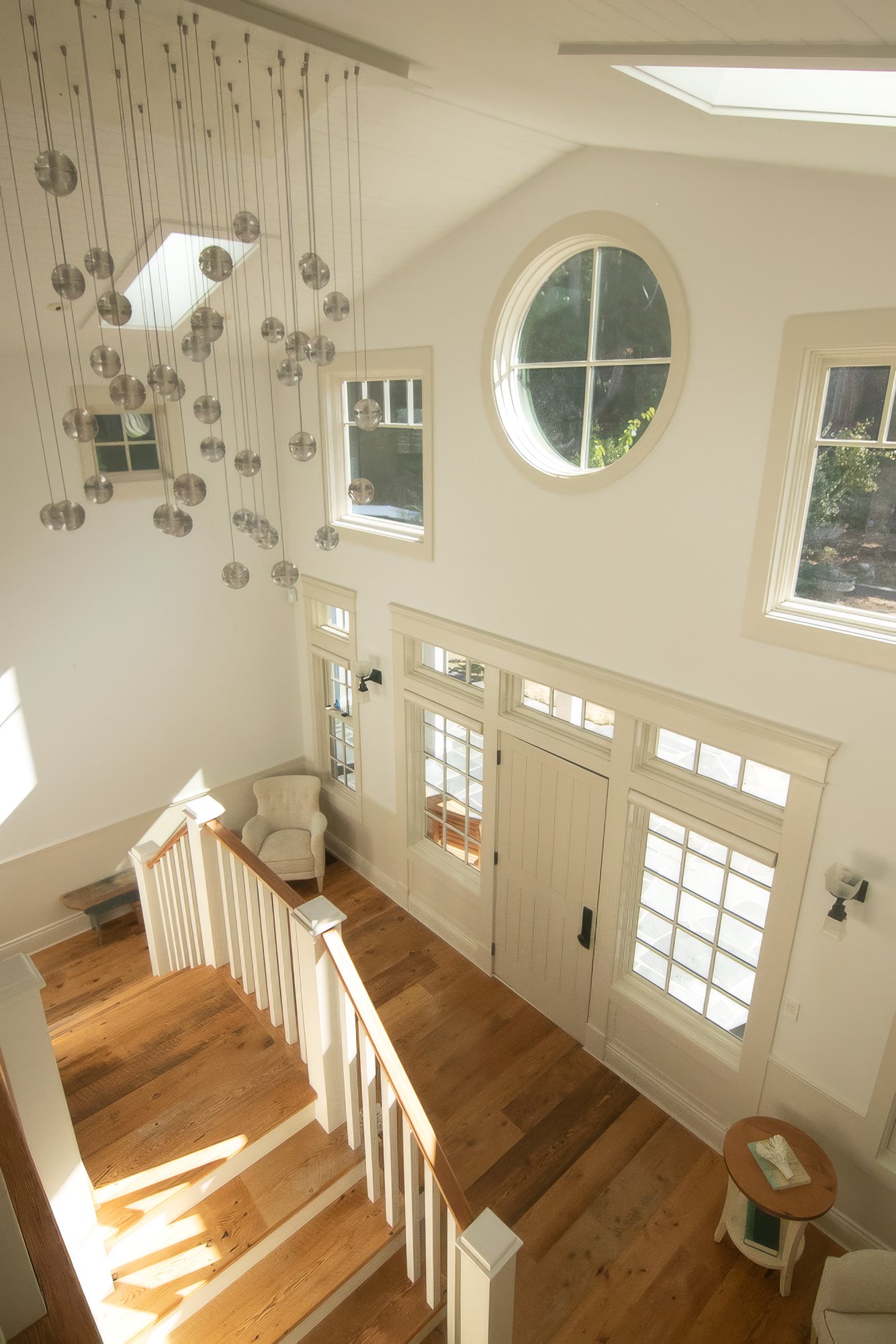 View down into the sunlit foyer from the landing, with a round window and a glass globe chandelier