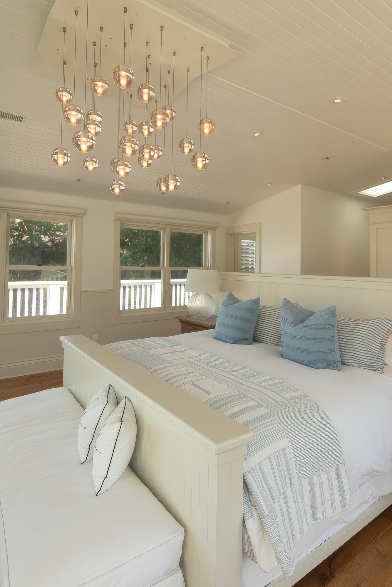 Primary suite with a glass globe chandelier over a king bed and windows onto the veranda