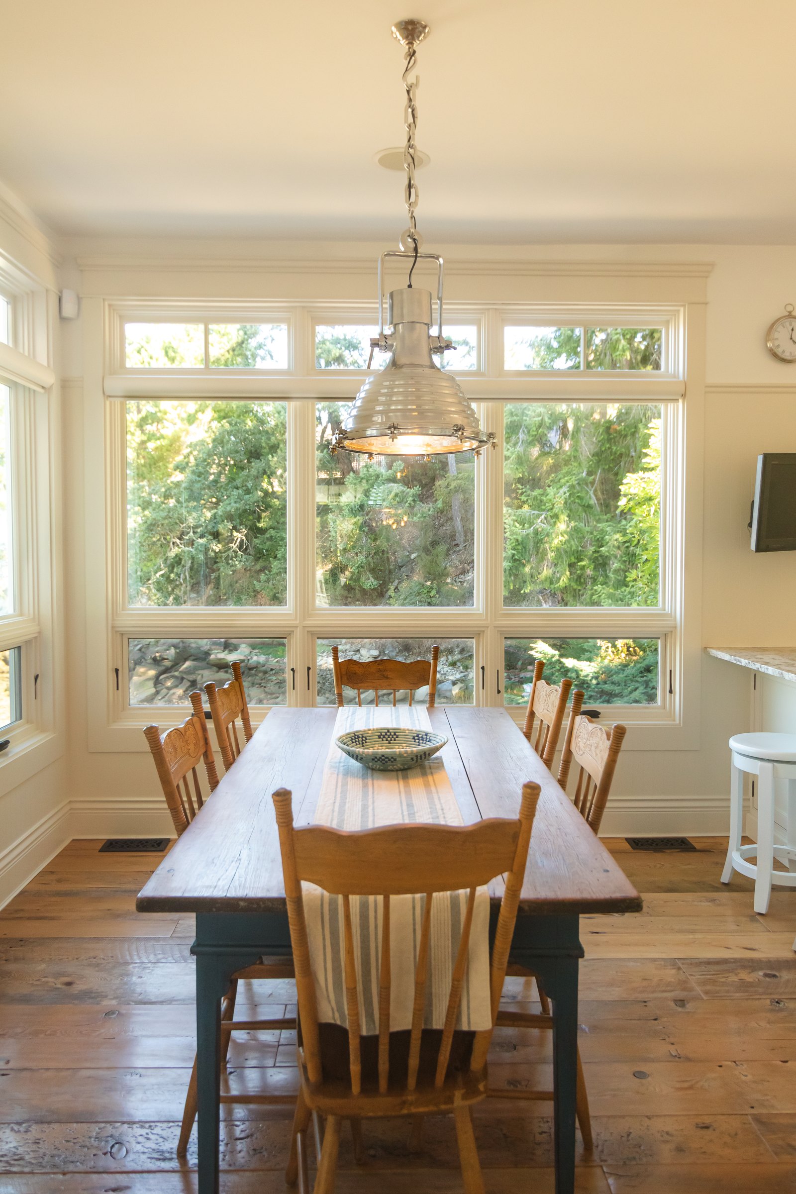 Farmhouse dining table beneath a ship's pendant light, set before tall windows onto the garden