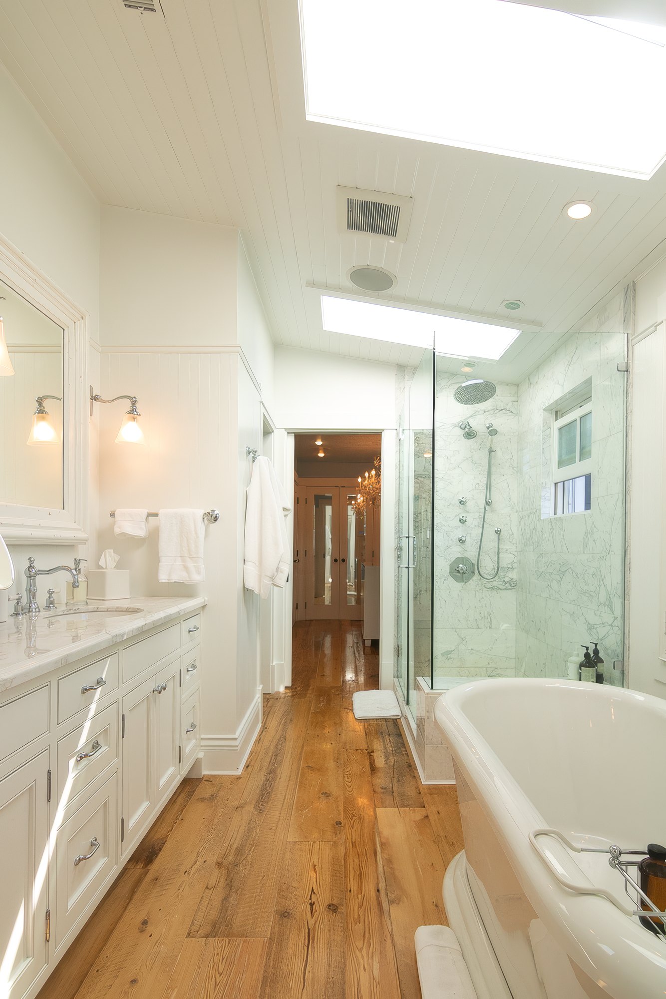 Primary bath with a freestanding soaking tub, Carrara marble shower, and skylights
