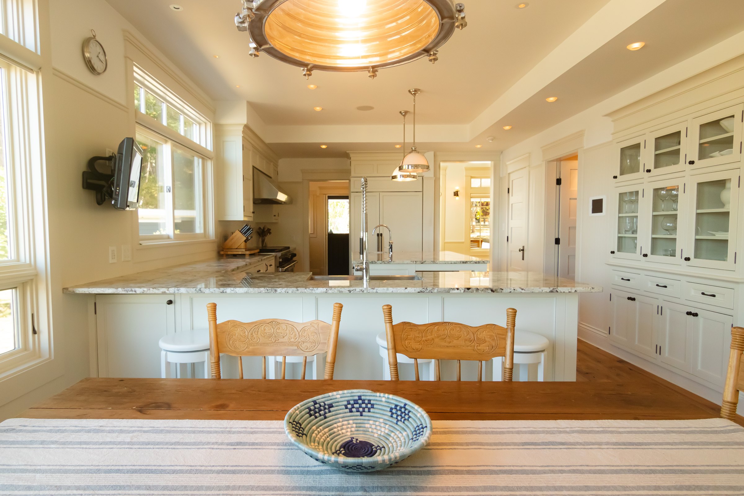 Bright white kitchen with a granite peninsula, glass-front cabinets, and a nautical pendant light