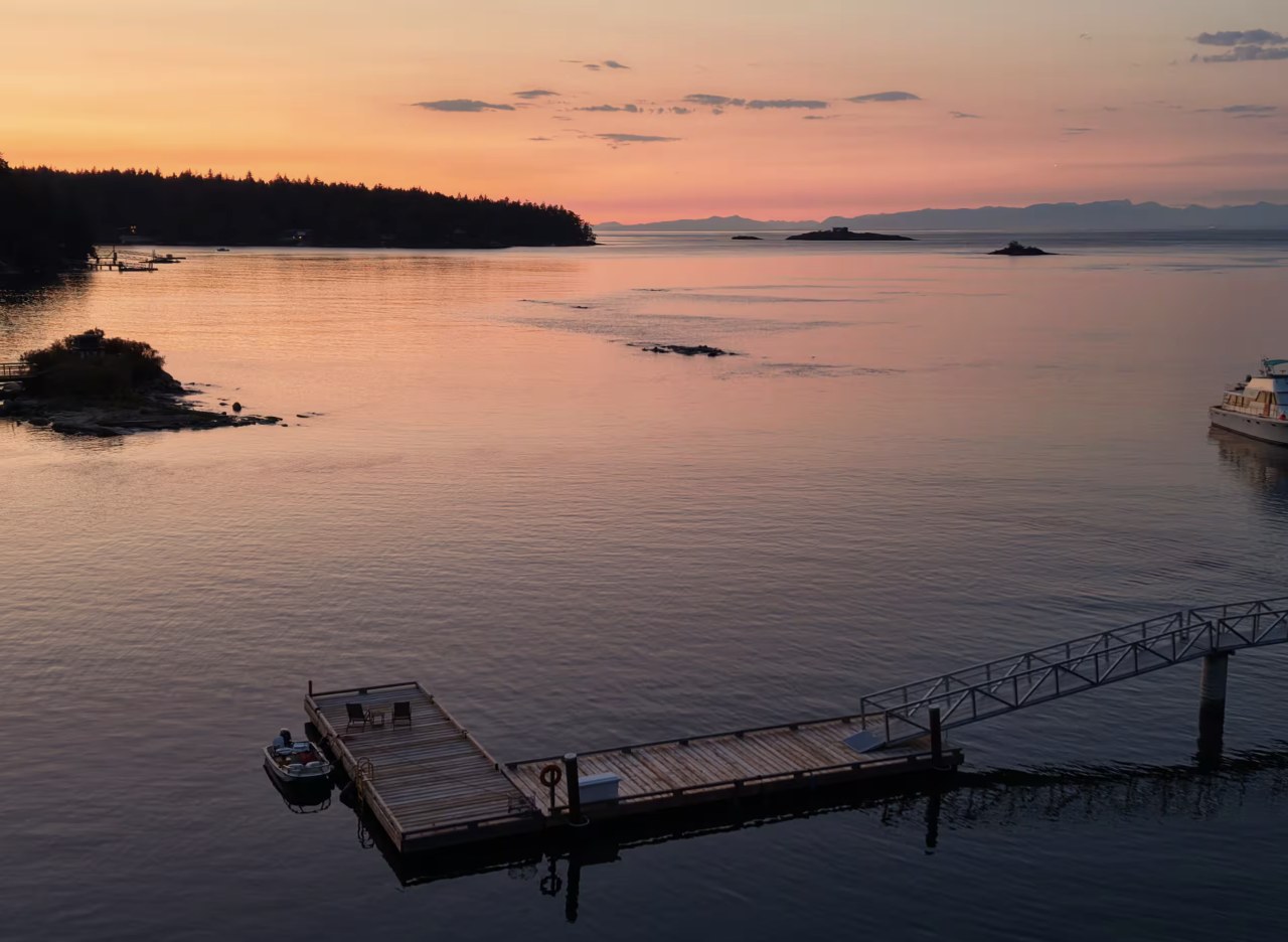 The private dock on glassy water at sunset, with islands and mountains on the horizon