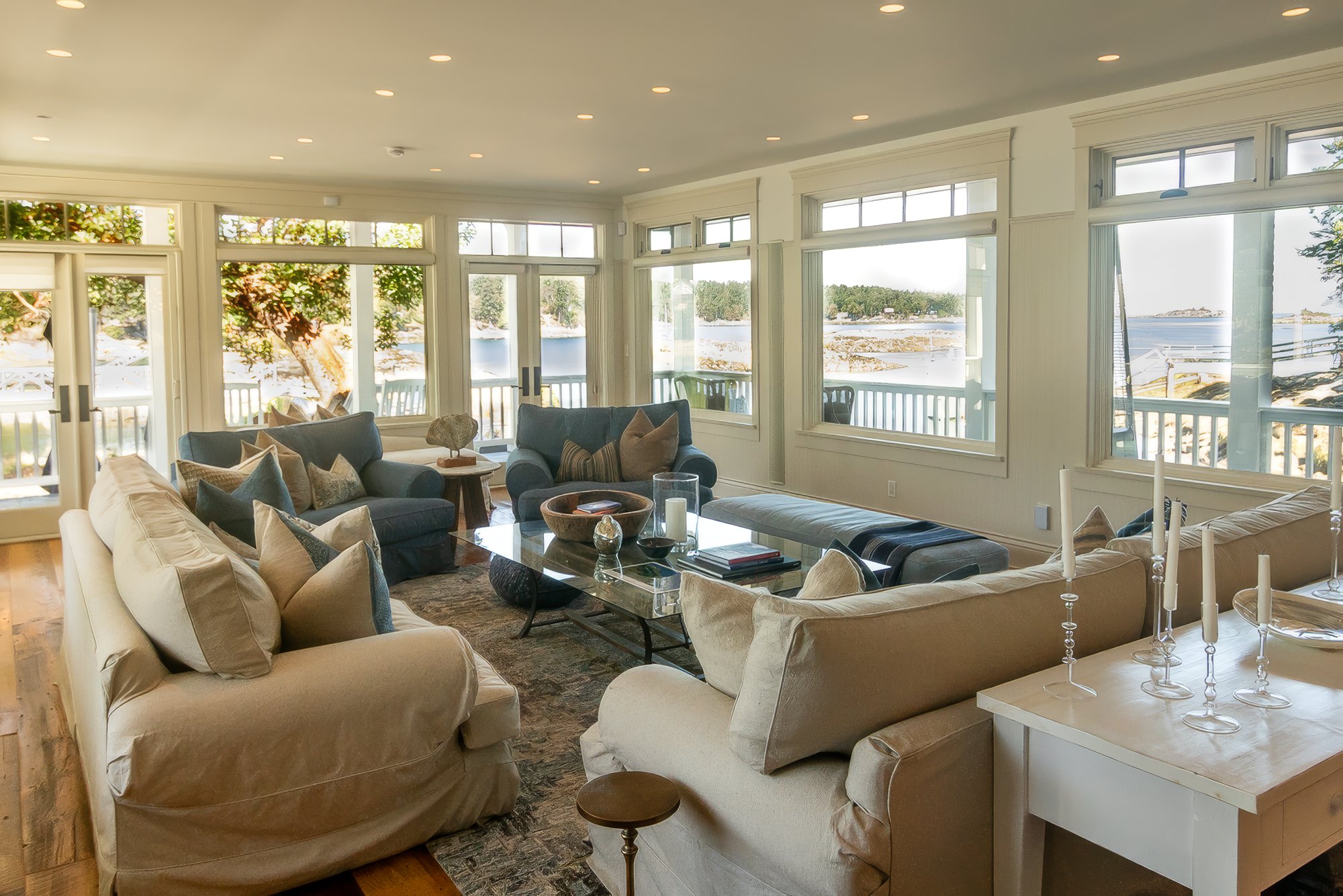 Great room with slipcovered sofas and walls of windows and French doors opening to the veranda and bay