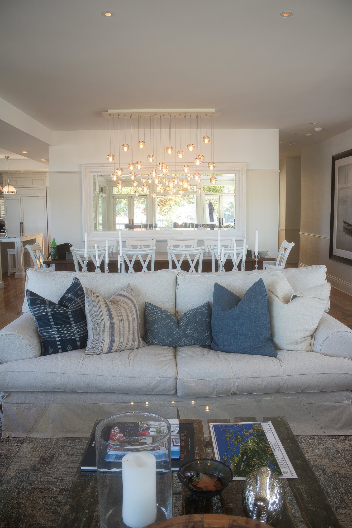 Long dining table for twelve beneath a glass globe chandelier, with a mirror reflecting the great room