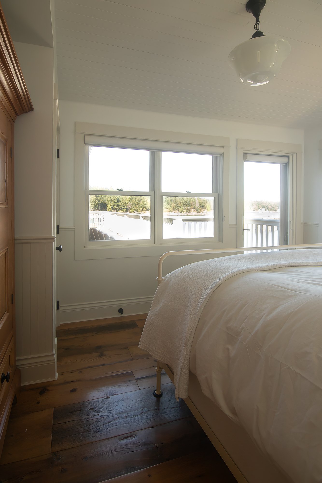 Guest bedroom with a white iron bed and a door opening onto a balcony above the water