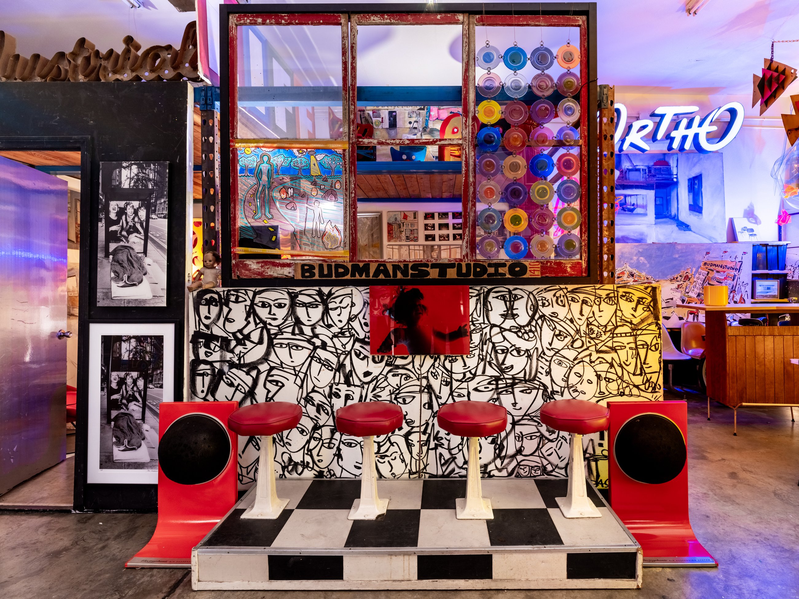 Checkerboard stage with red stools and speakers under the Budman Studio sign
