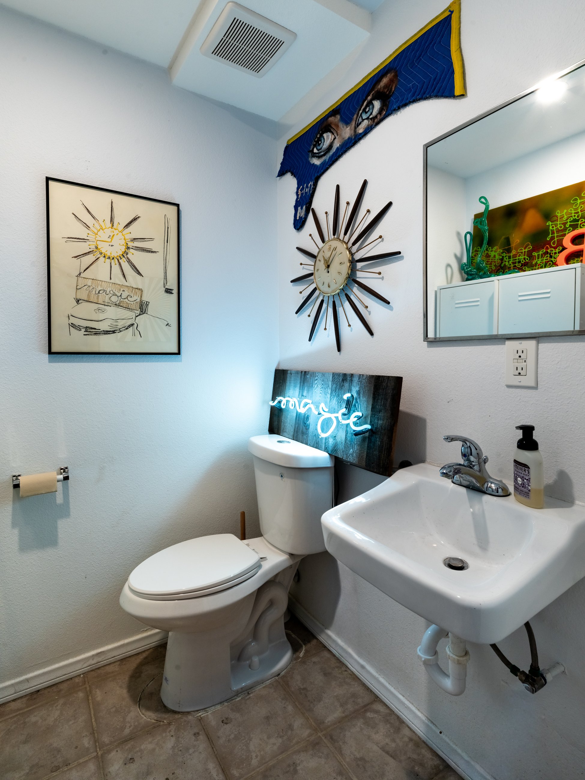 Bathroom with a neon magic sign and a sunburst clock