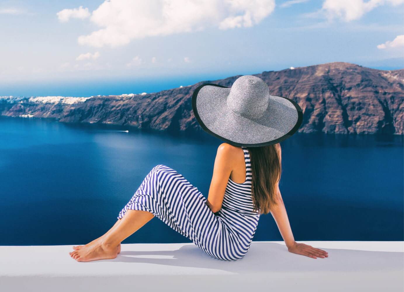 Lady in a hat sitting on a white platform overlooking the sea
