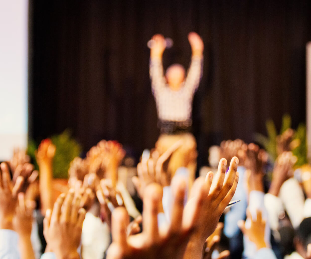 People in the audience and a man onstage raising their hands