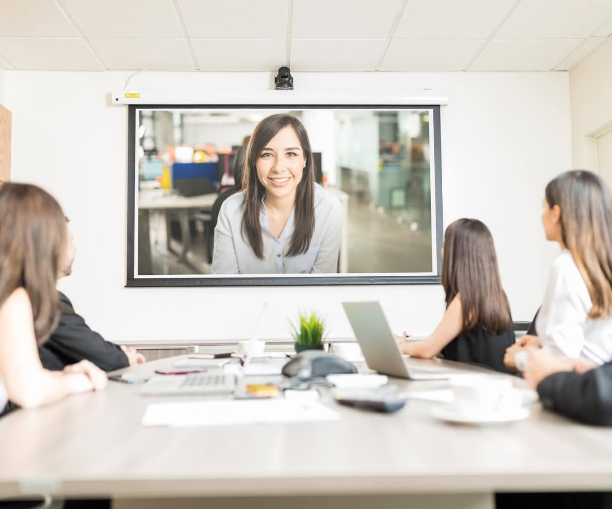 People attending a hybrid meeting inside a boardroom with a projection screen in the front