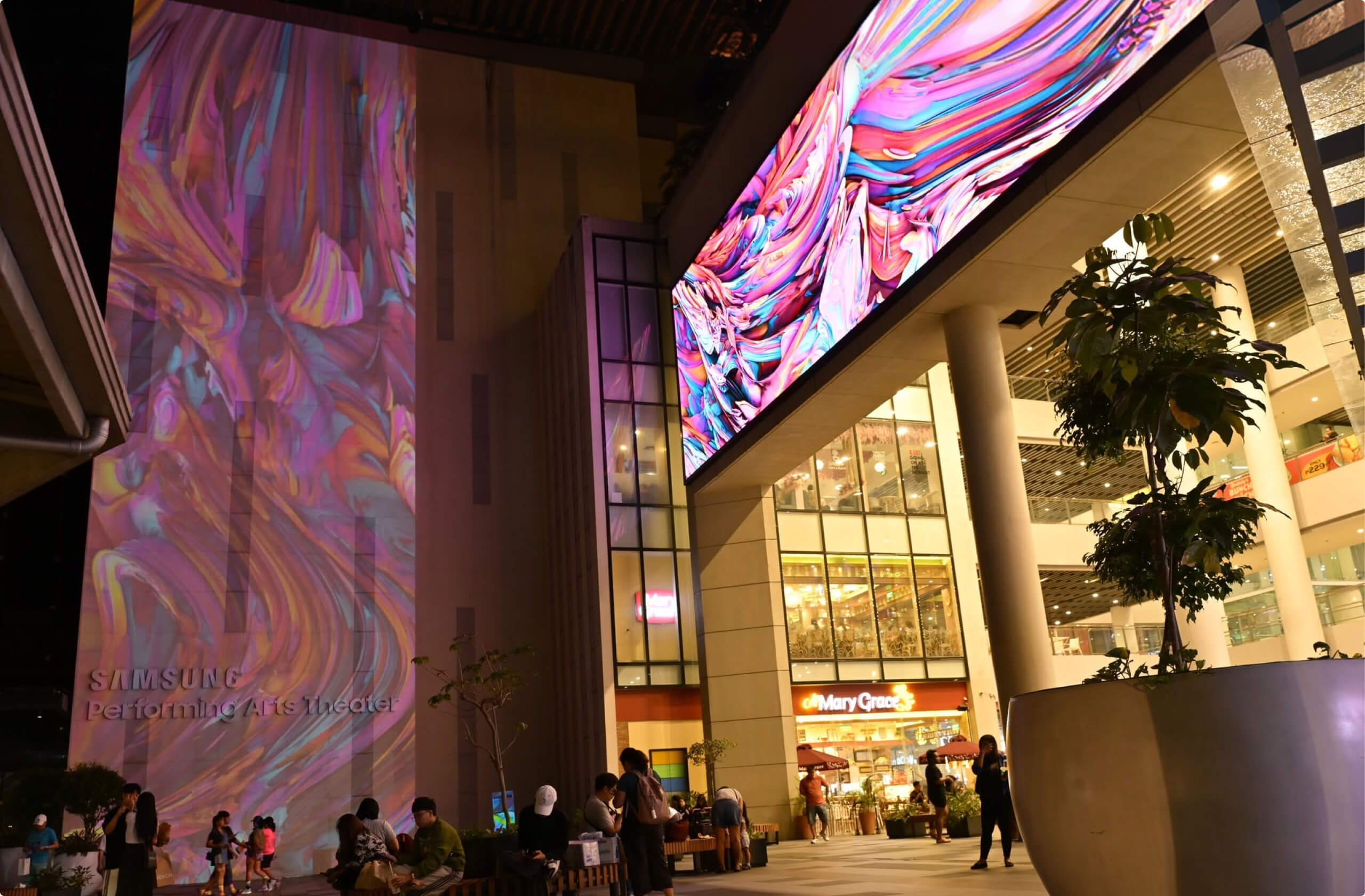 Colorful abstract light projections on Samsung Performing Arts Theater at night with people nearby.