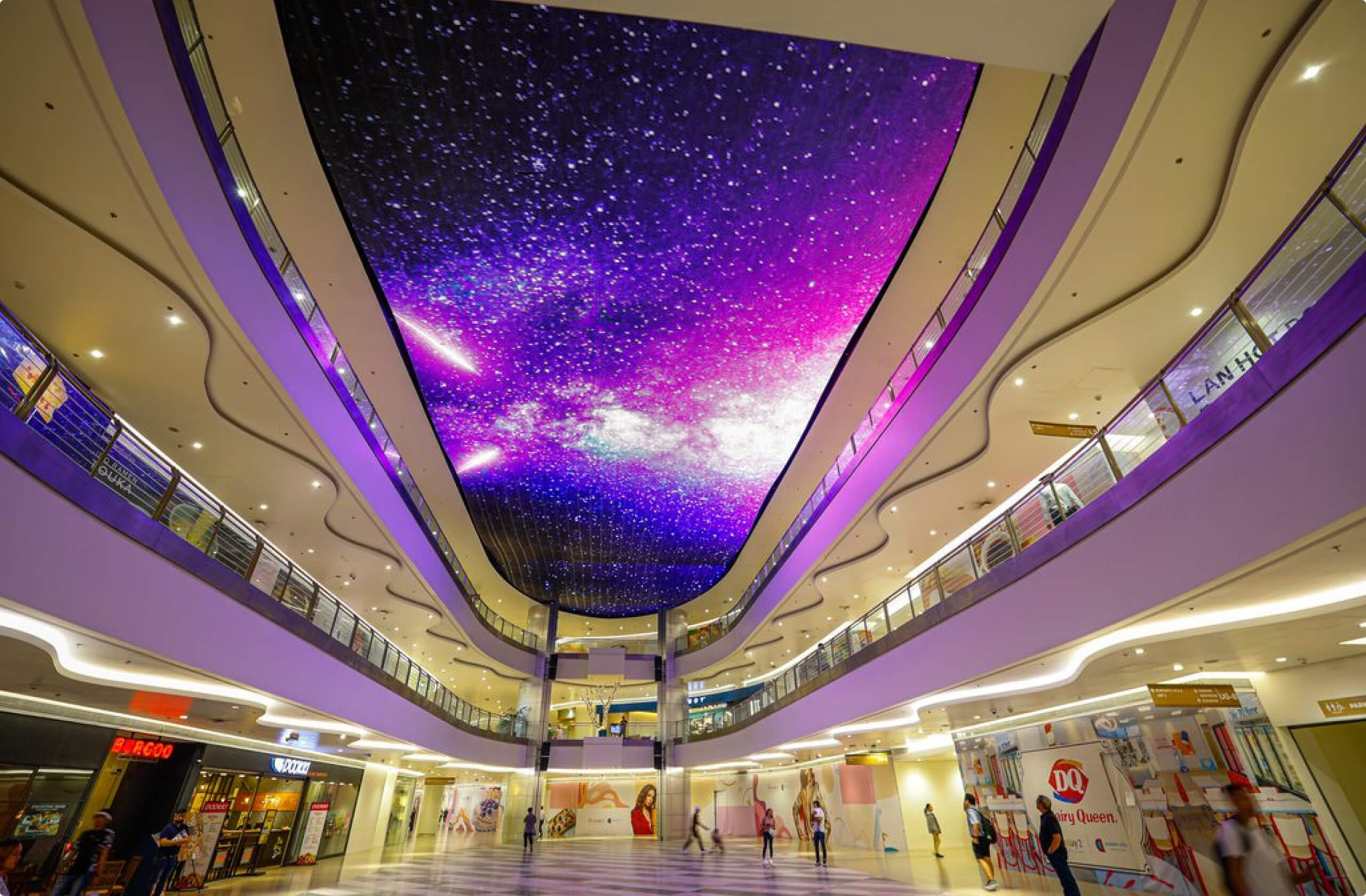 Spacious mall interior with two levels and a vibrant purple LED ceiling resembling a starry night sky.